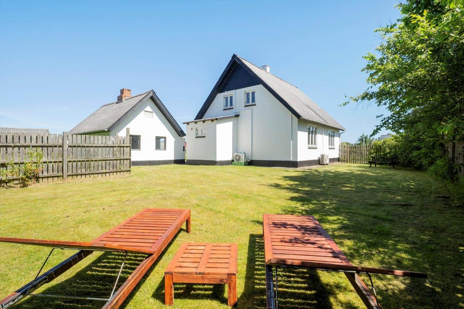Zwei Häuser mit Garten, Sonnenliegen und Bäumen. Hinterhof mit Holzgeländer.