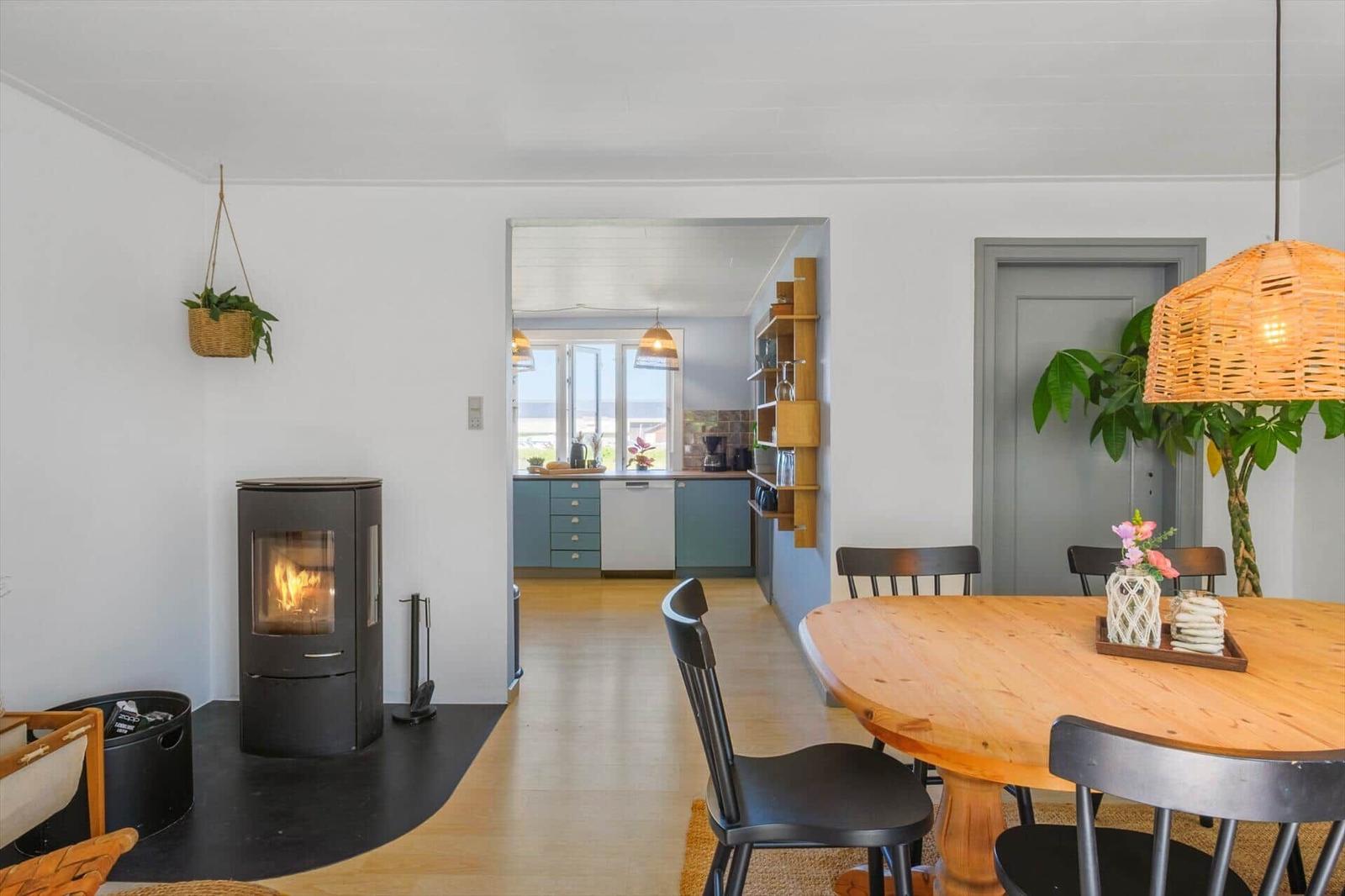 Essbereich mit Holztisch, schwarzen Stühlen und Kamin. Küche mit blauen Schränken sichtbar.