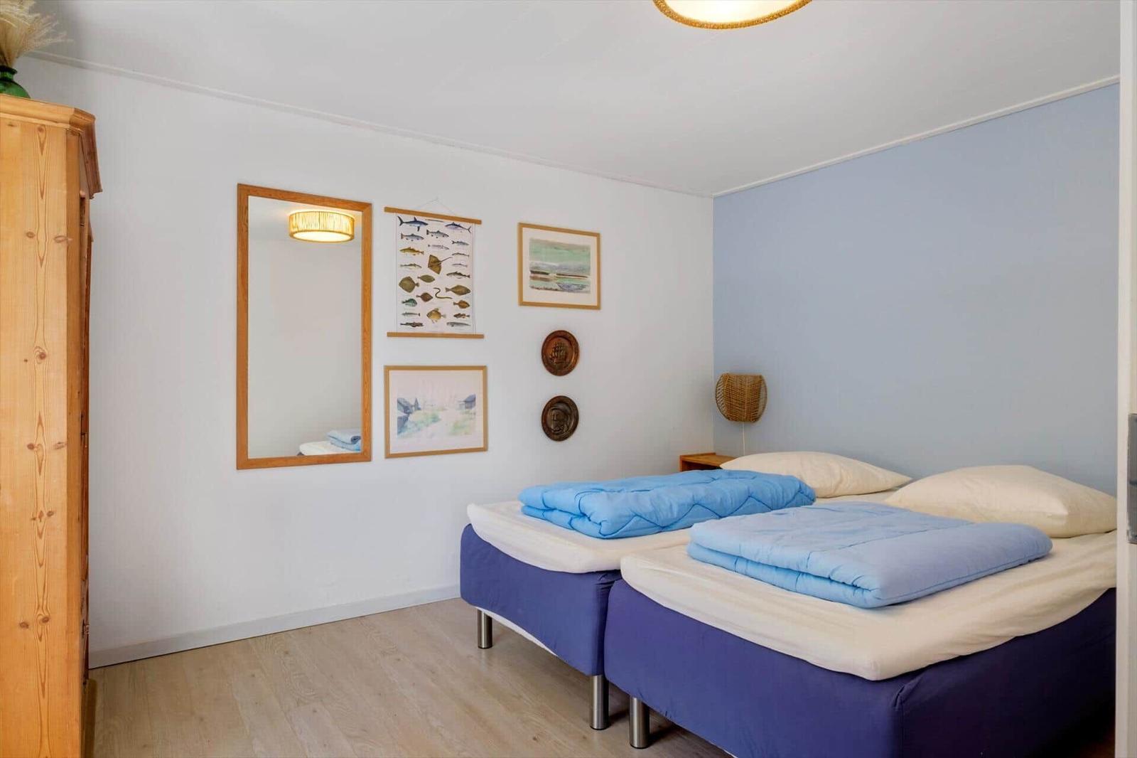 Zwei Betten mit blauen Decken, Wandbilder und Spiegel in einem Raum mit Holzboden und blauer Wand.