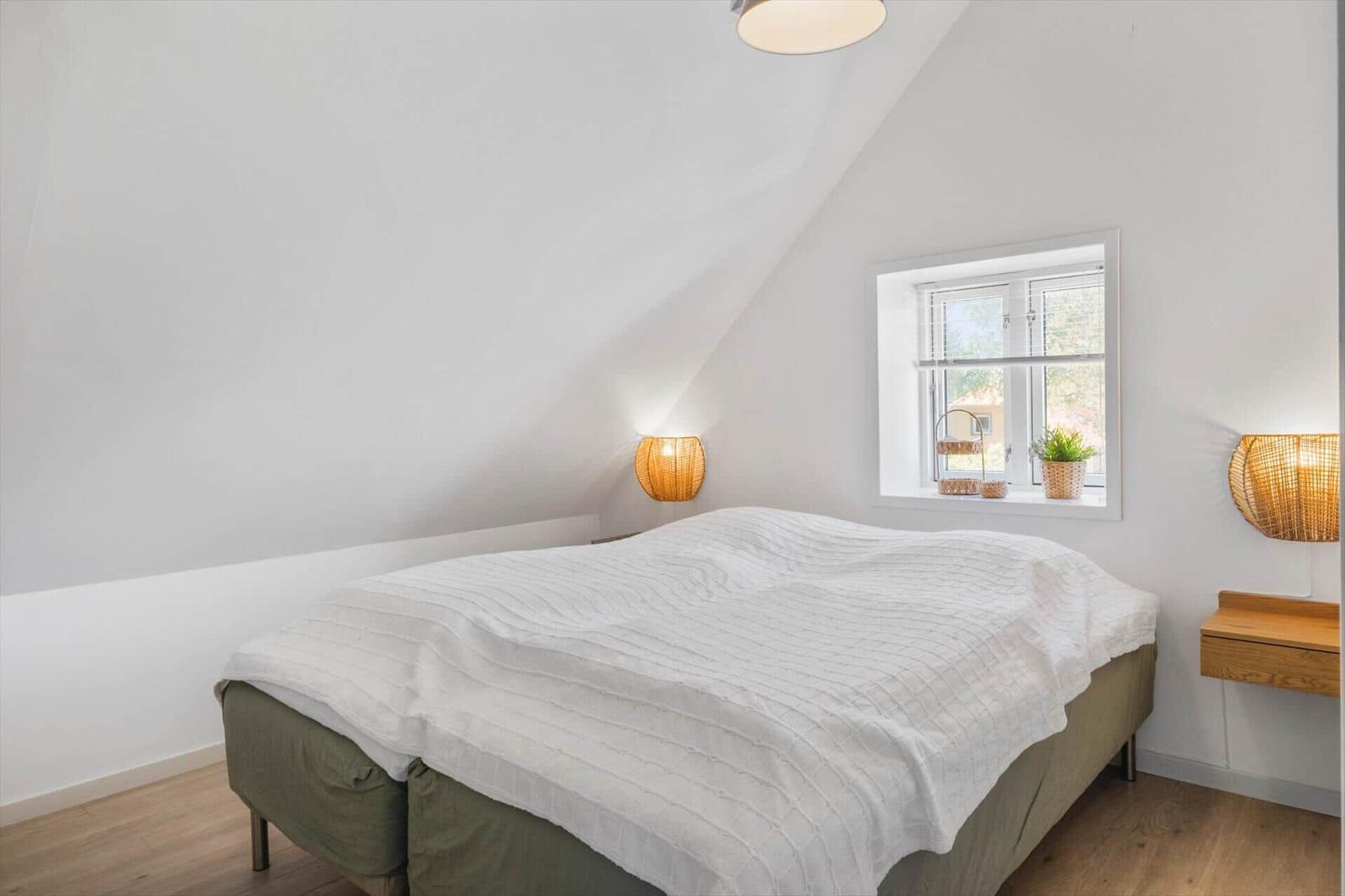 Schlafzimmer mit Dachschrägen, Bett, Fenster und Nachttischen mit Lampen.