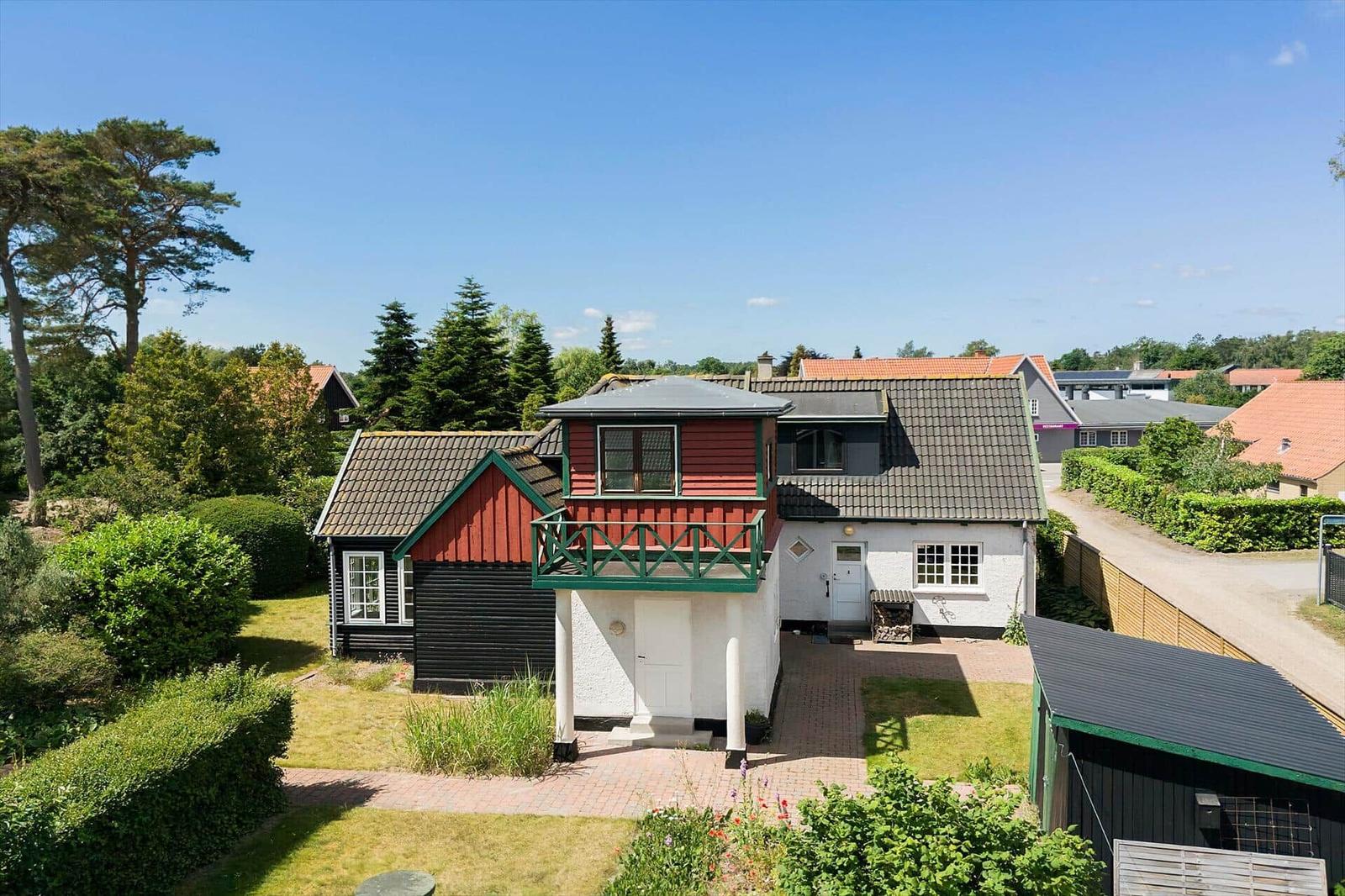 Ein zweistöckiges Haus mit Balkon, umgeben von Grün und Bäumen unter blauem Himmel.