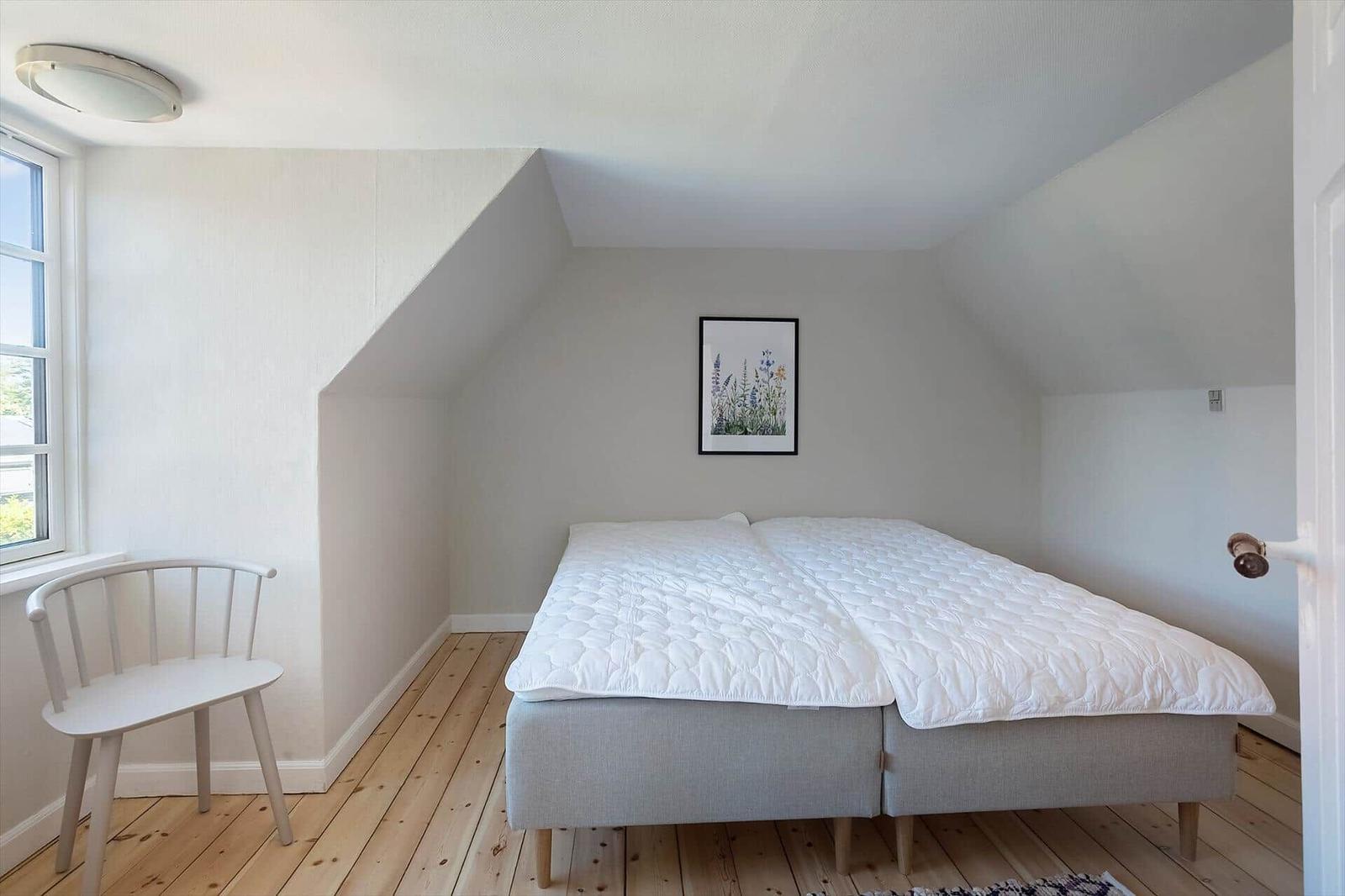 Schlafzimmer mit Dachschrägen, Bett, Stuhl und Fenster.