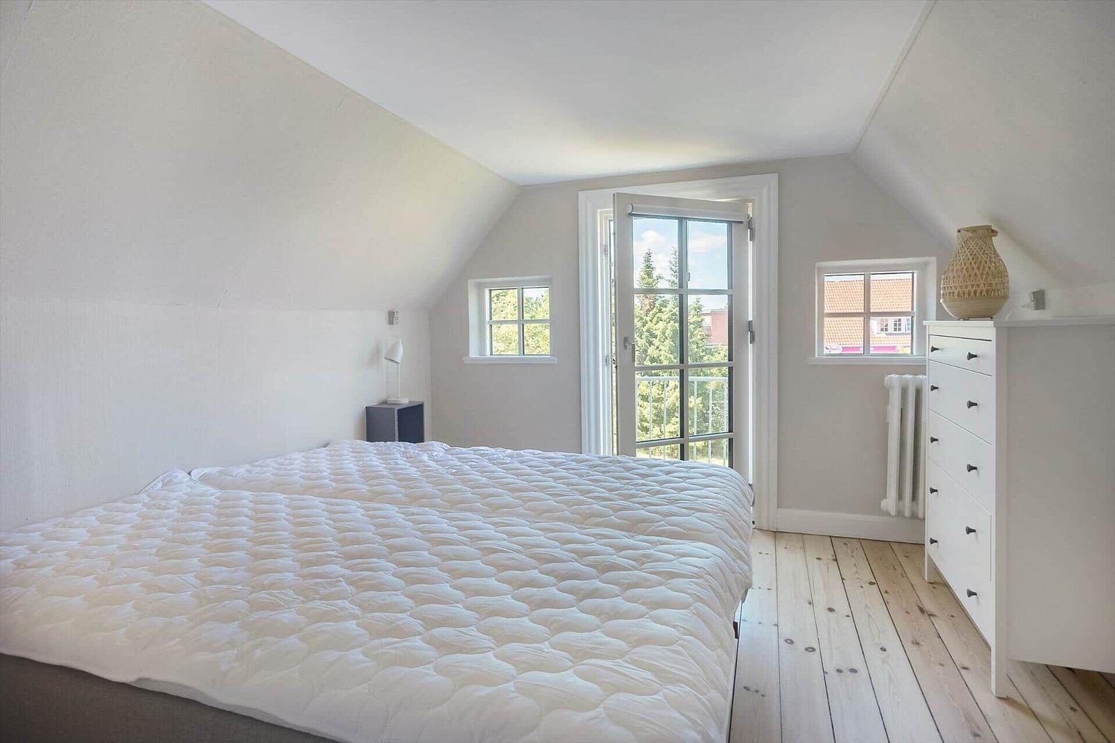 Schlafzimmer mit Dachschrägen, Bett, Schrank und Fenster zur Aussicht.
