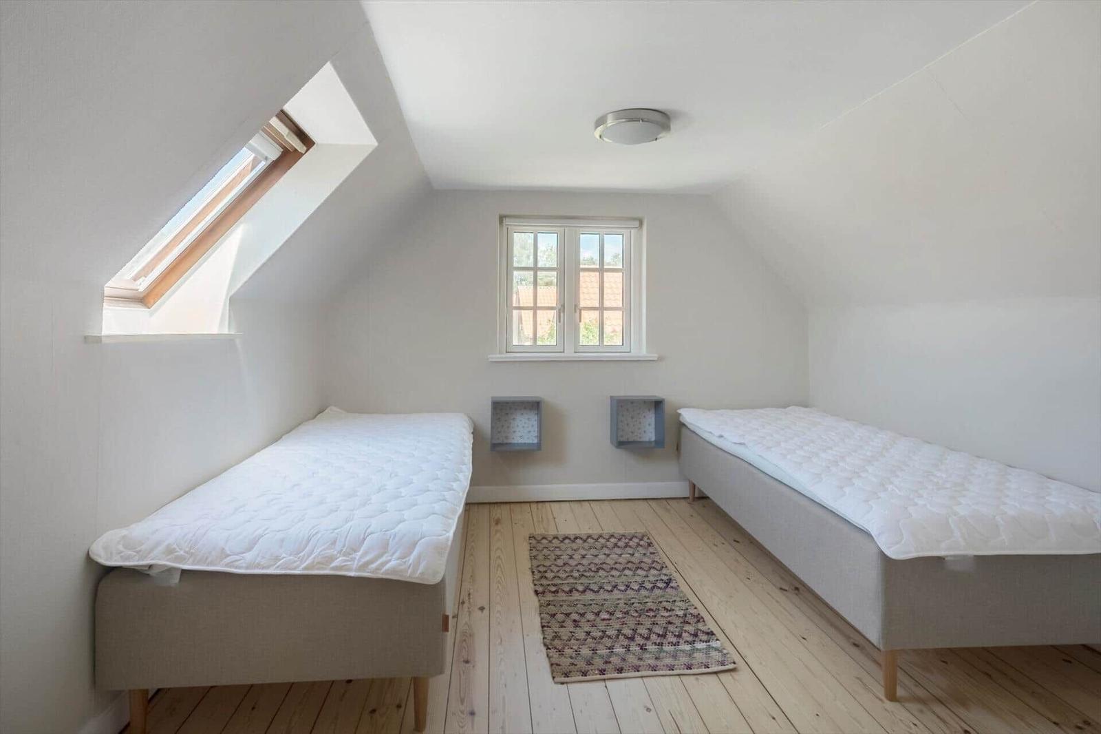 Zwei Einzelbetten in einem Dachgeschosszimmer mit Holzboden und Fenstern.