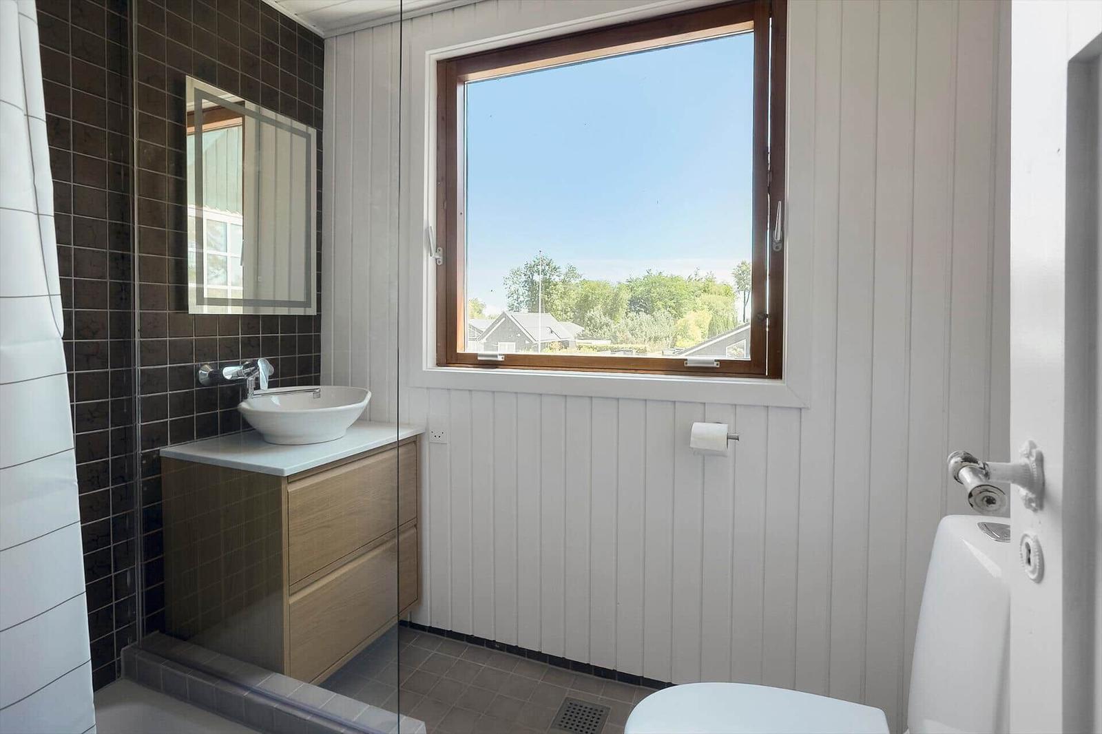 Badezimmer mit Waschbecken, Spiegel und großem Fenster mit Blick auf Außenbereich.