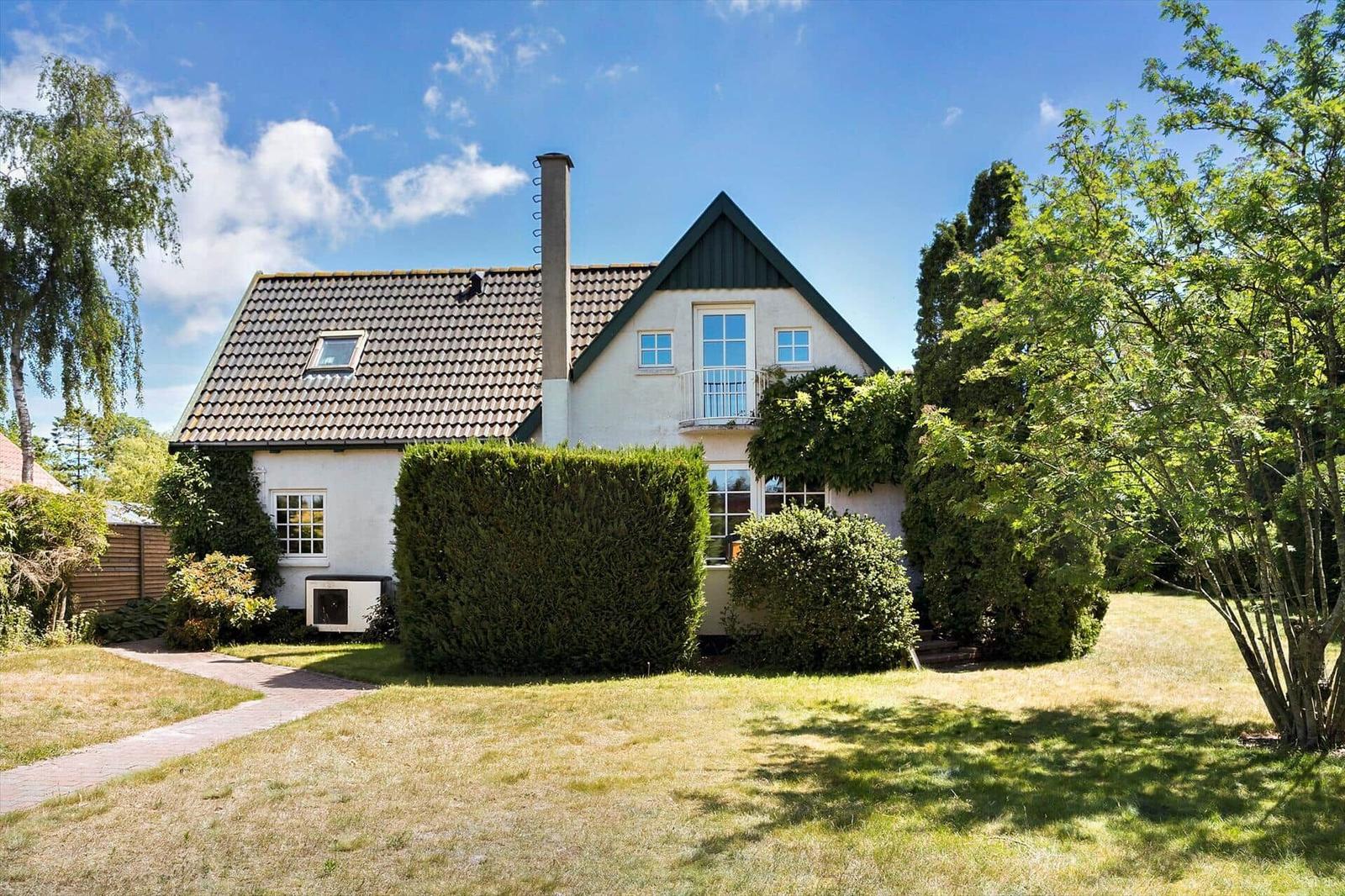 Haus mit Garten, Balkon und Schornstein unter blauem Himmel.
