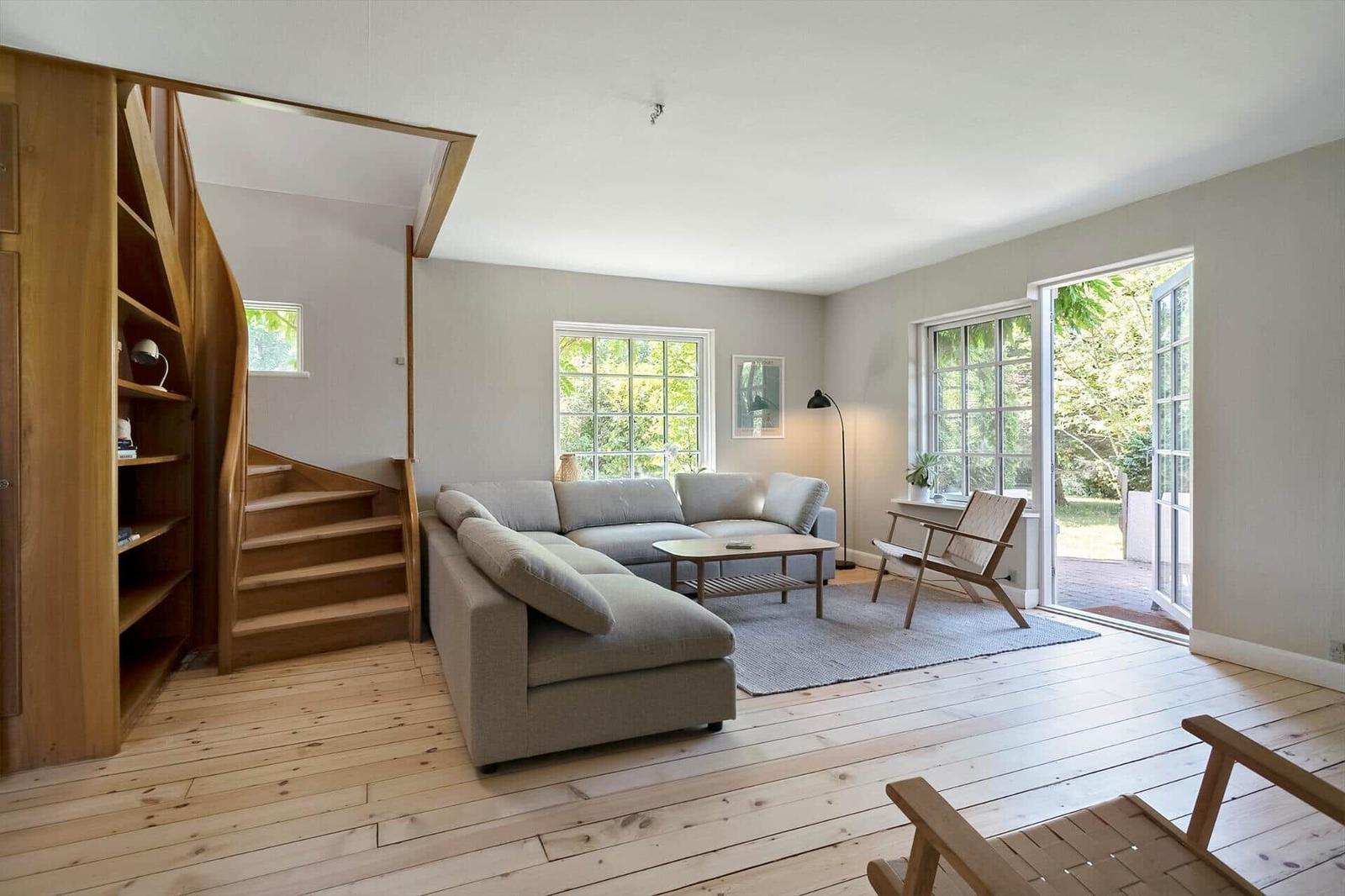 Wohnzimmer mit Sofa, Tisch und Sessel. Holzdielenboden und Fenster zur Außenterrasse.
