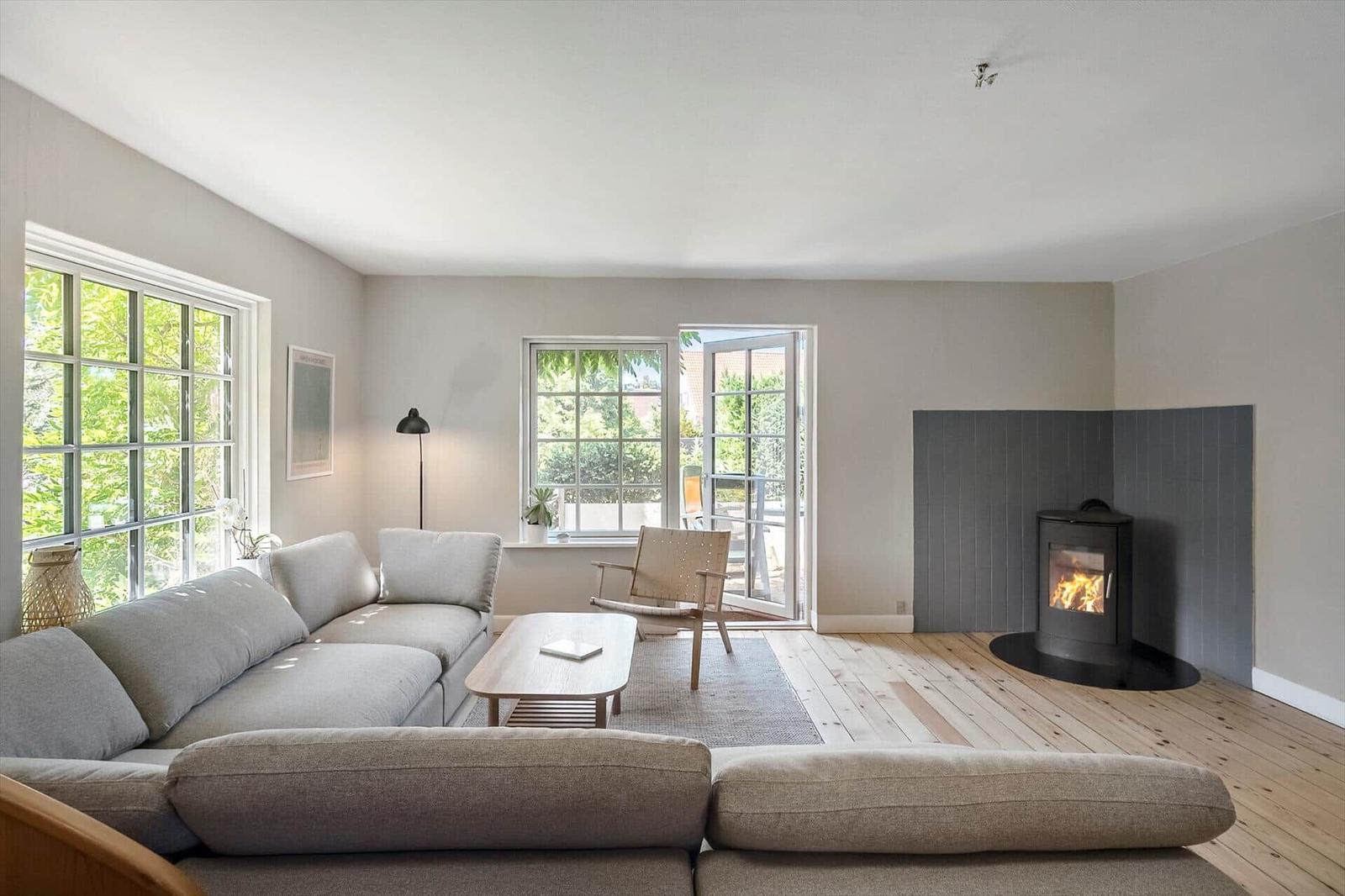 Wohnzimmer mit Sofa, Kamin und Fenstern zum Garten.
