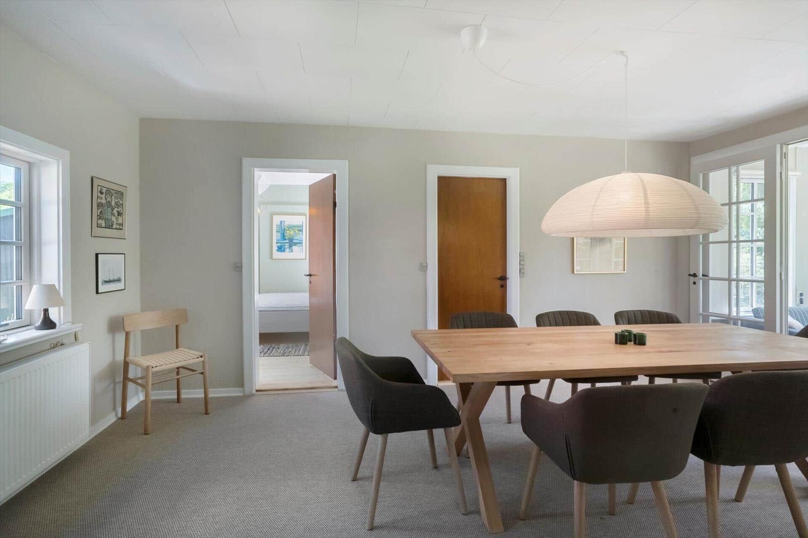Esszimmer mit Holztisch, Stühlen und Deckenleuchte. Durchgang zu Schlafzimmer und Tür.