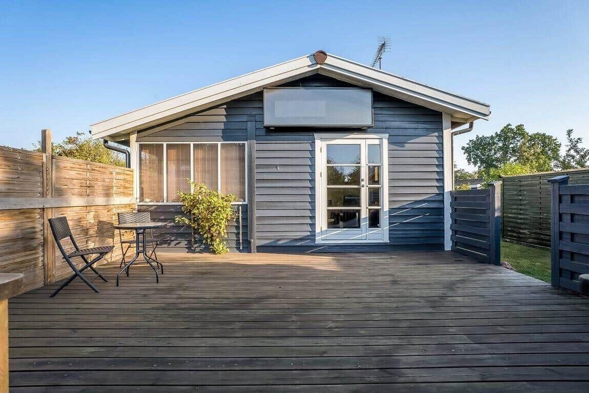 Haus mit Holzterrasse, Gartentür und Sitzgelegenheit.