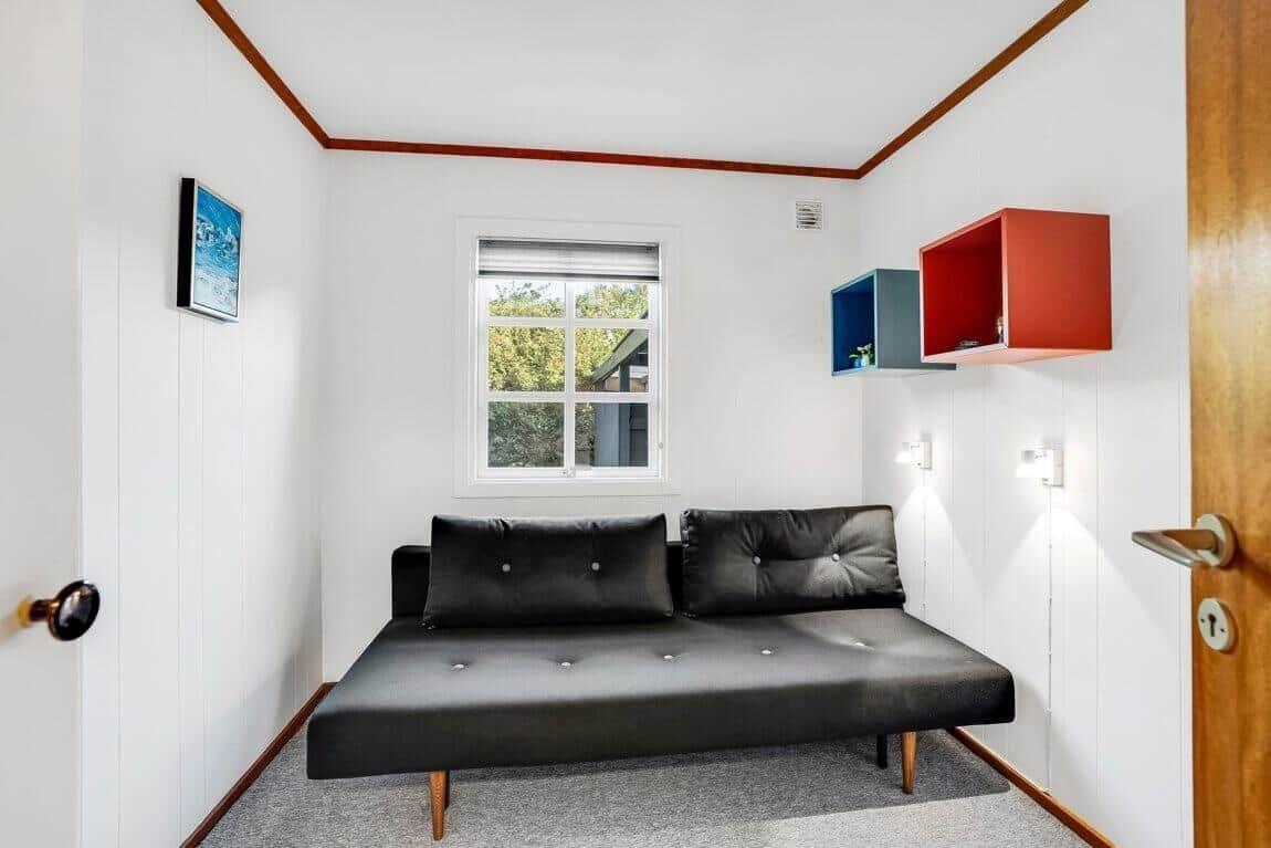 Schwarzes Sofa mit Kissen, Fenster und Wandregale in einem Raum mit weißen Wänden.