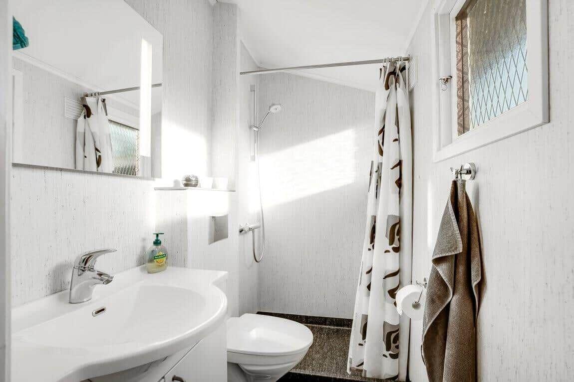 Badezimmer mit Dusche, Waschbecken und Toilette. Duschvorhang und Handtuch hängen an der Wand.