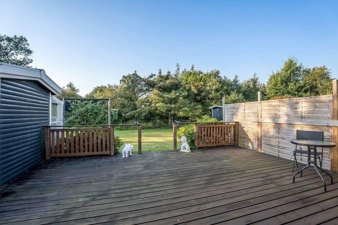 Terrasse mit Tisch, Zaun und Garten. Hintergrund: Bäume und klarer Himmel.