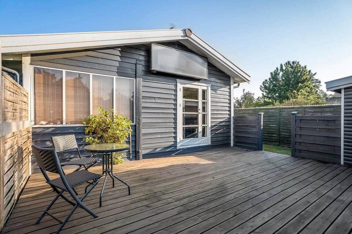 Terrasse mit Tisch und Stühlen vor einem Holzhaus mit Fenstern und Tür.