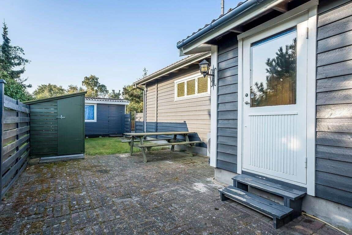 Haus mit Terrasse, Tisch, Bank und Gartenhütte. Eingangstür mit Glasfenster.