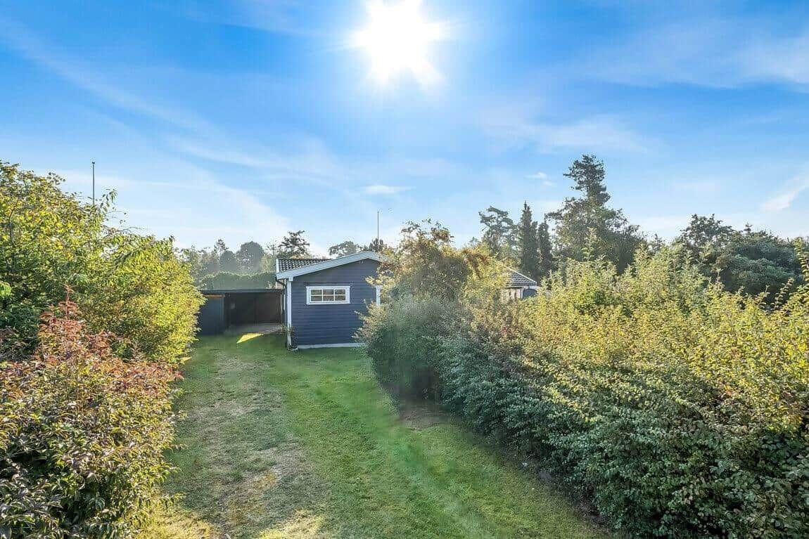 Ein kleines Haus mit Garten und umgebenden Bäumen unter blauem Himmel.