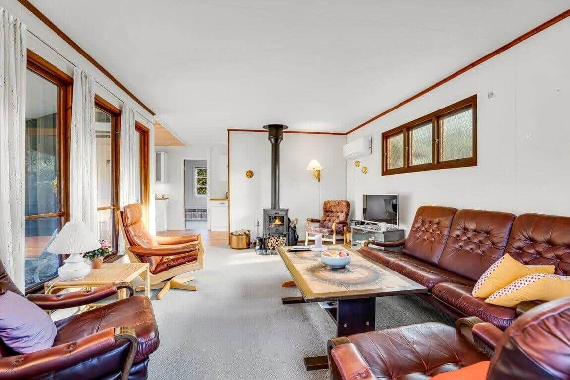 Wohnzimmer mit braunen Ledermöbeln, Kamin und großen Fenstern.