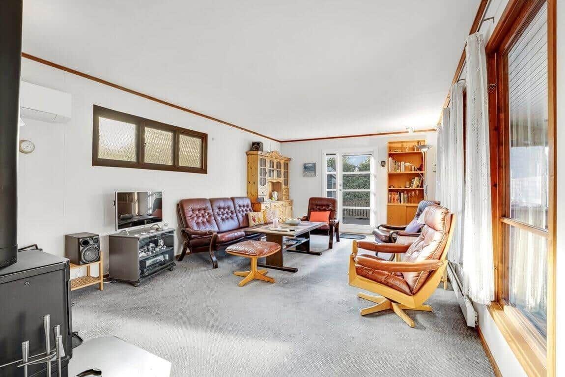 Wohnzimmer mit Ledersofa, Sessel und Fernseher. Fenster und Tür führen nach draußen.