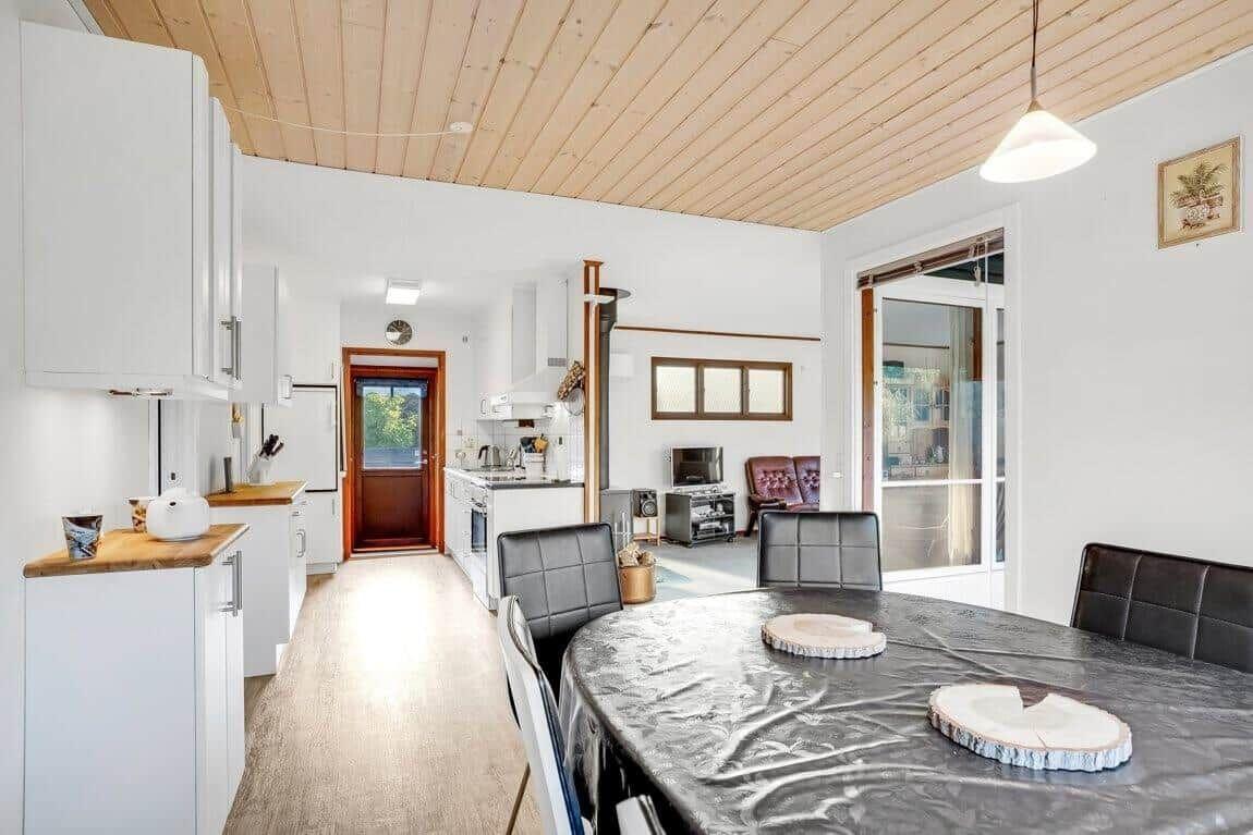 Essbereich mit runder Tisch und schwarzen Stühlen, Küche und Wohnbereich mit Holzdecke.