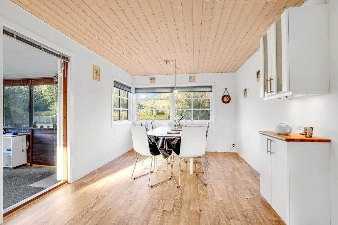 Esszimmer mit Holzdecke, Tisch, Stühle und Fenster. Küche mit Arbeitsplatte und Schränken.