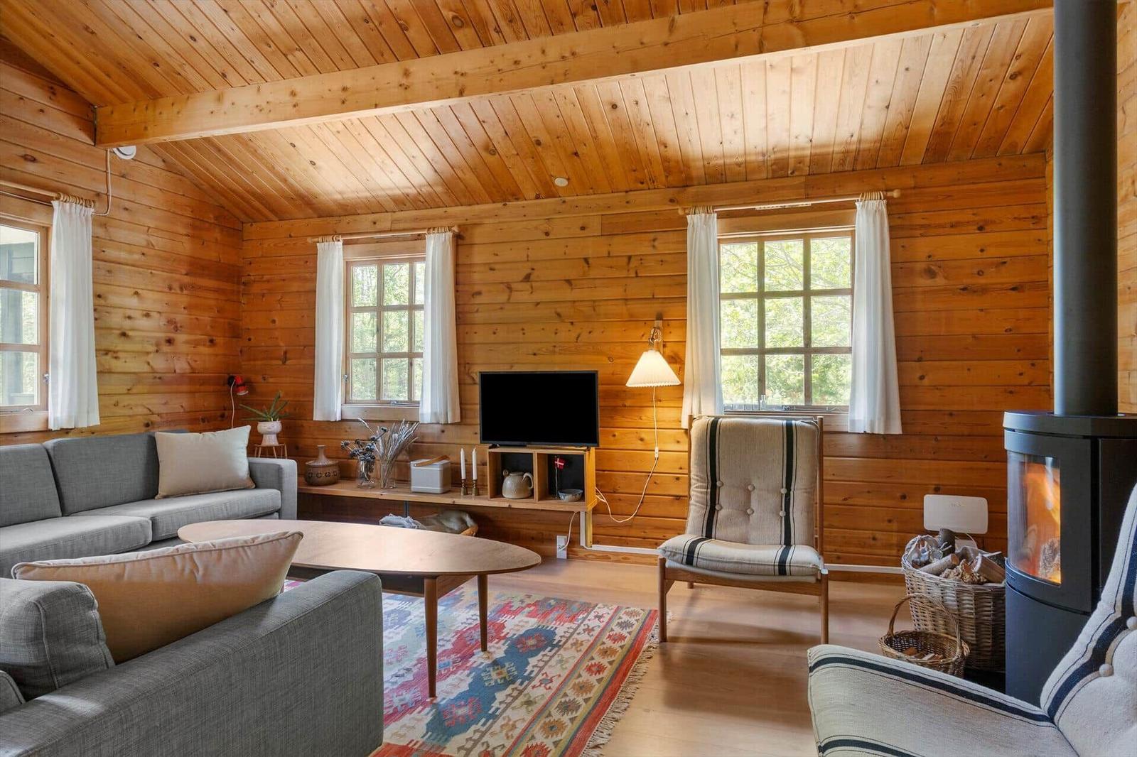 Wohnzimmer mit Holzwand, Sofa, Sessel, Fernseher und Kaminofen.
