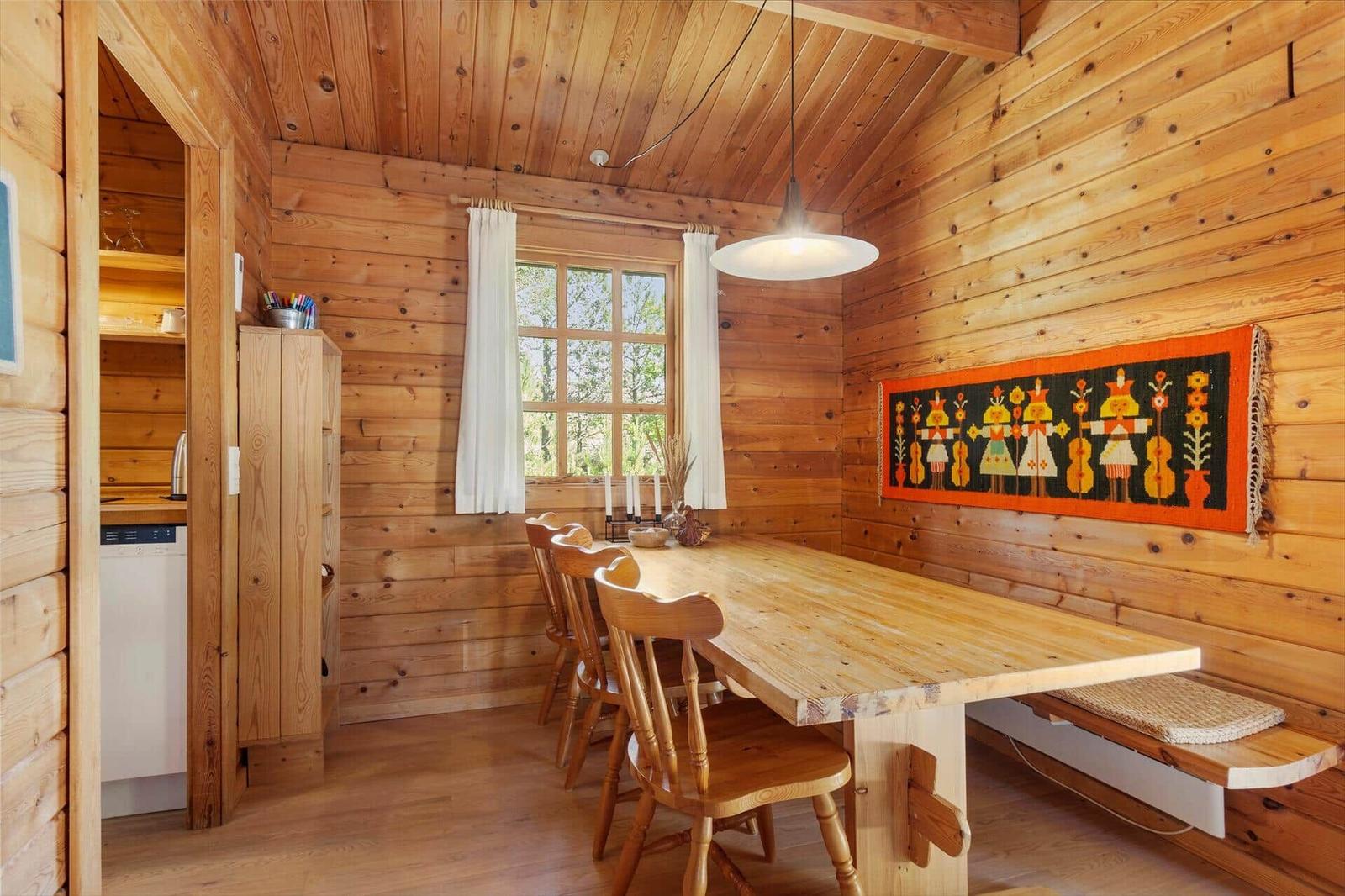 Esszimmer mit Holztisch, Stühlen und Wandteppich. Fenster mit weißen Vorhängen.