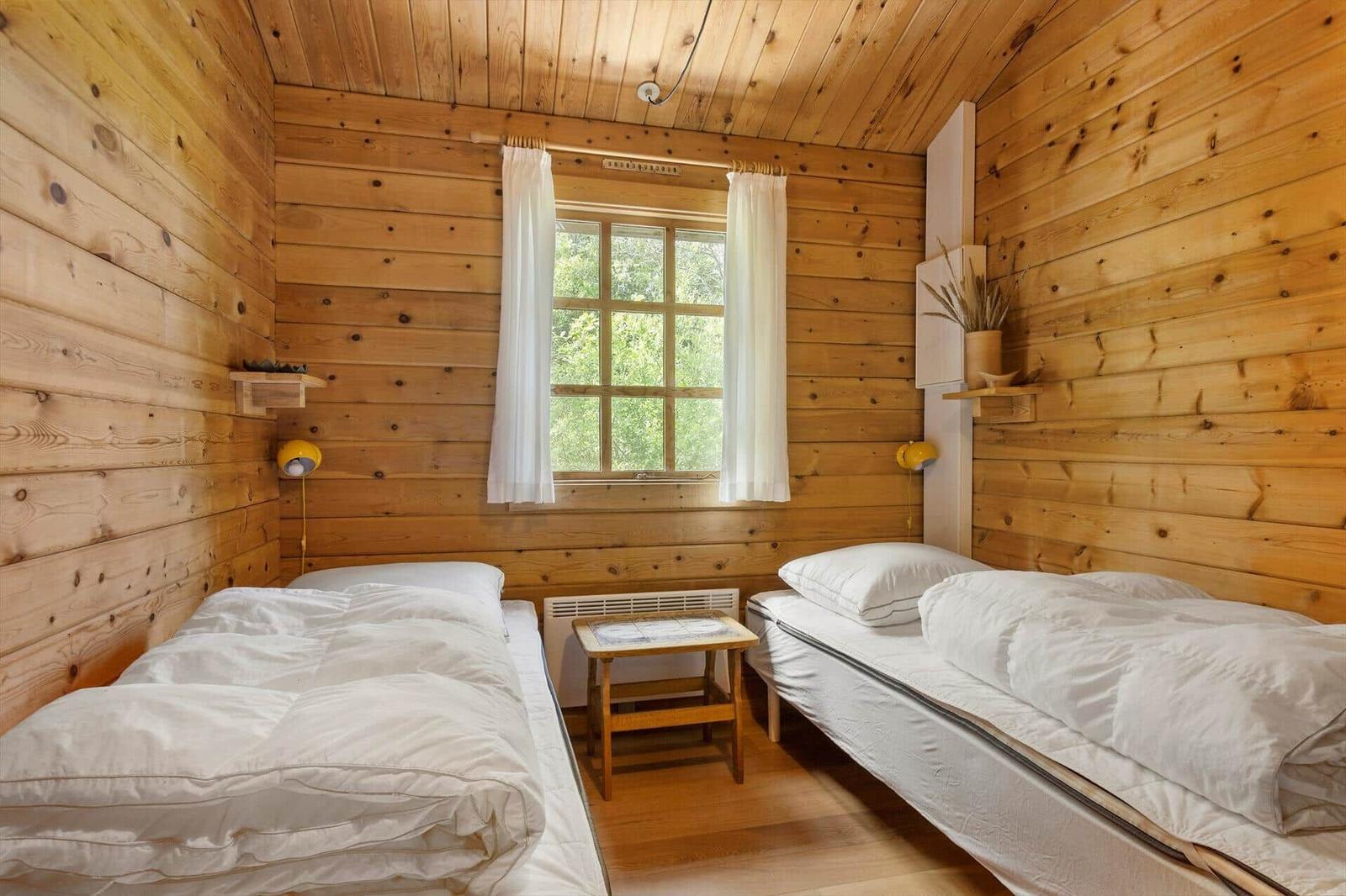 Zwei Einzelbetten mit weißen Bettwäschen, Holzwand und Fenster mit weißen Vorhängen.