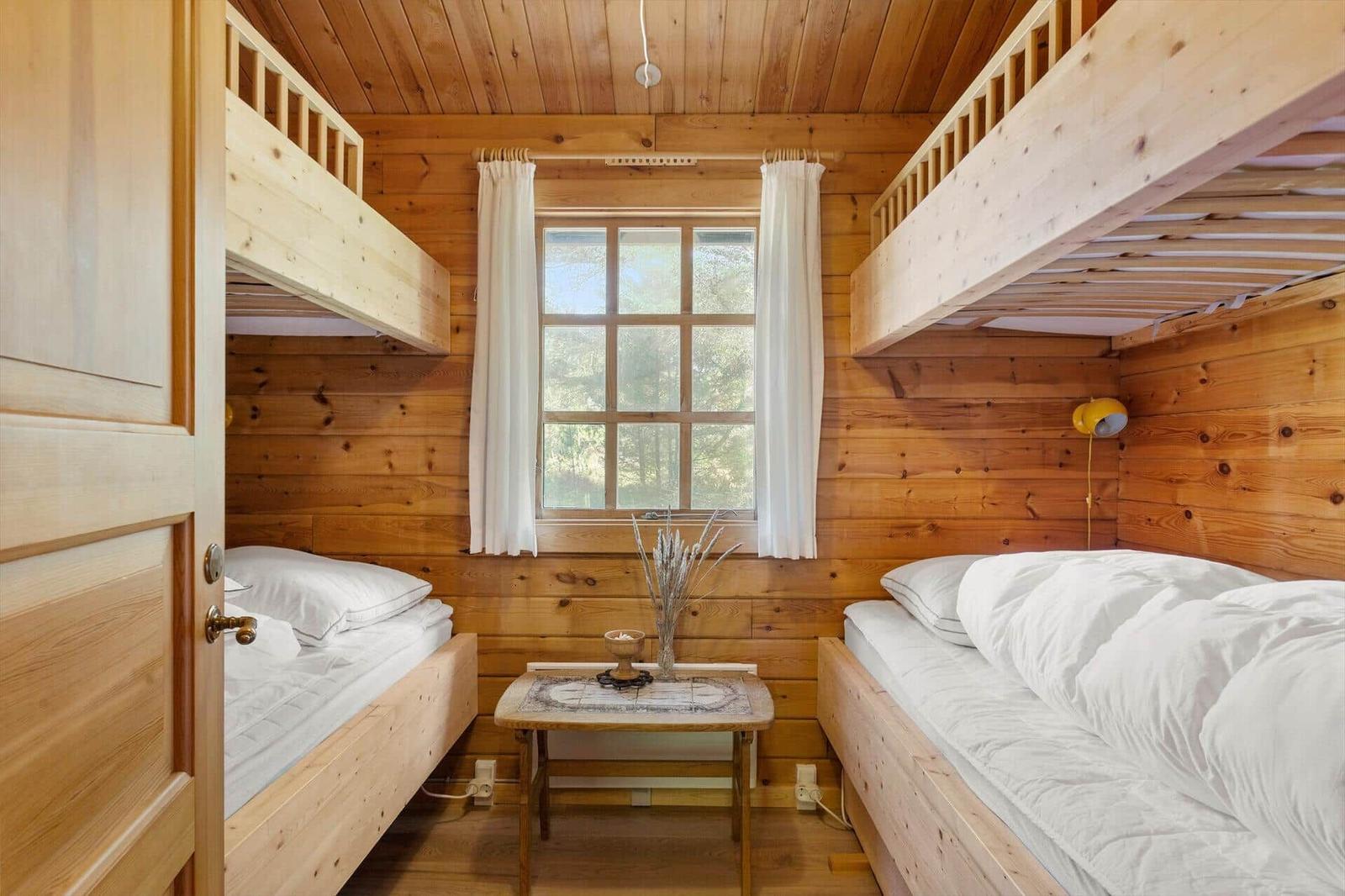 Zimmer mit zwei Etagenbetten, Holzwand und Fenster mit weißen Vorhängen.