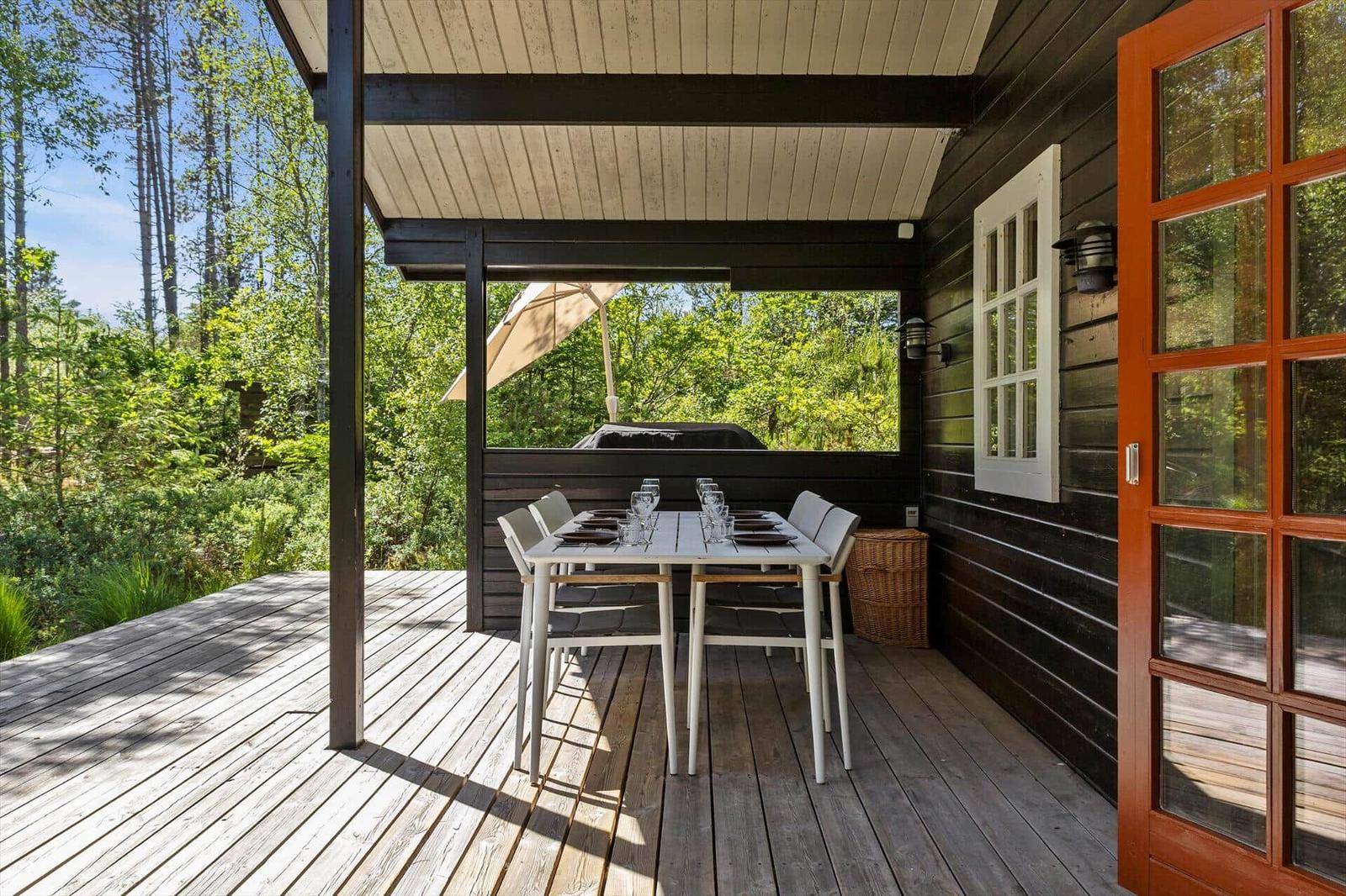 Terrasse mit Tisch und Stühlen, Blick in den Wald. Holzwand und rote Tür.