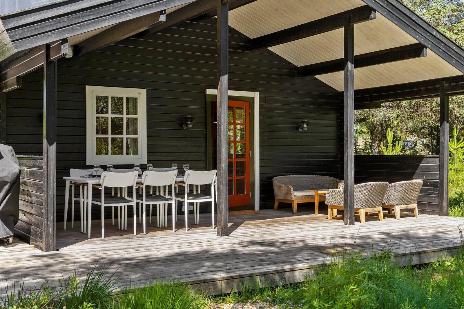 Terrasse mit Tisch, Stühlen und Sitzgruppe. Dunkle Holzwände und rote Tür.