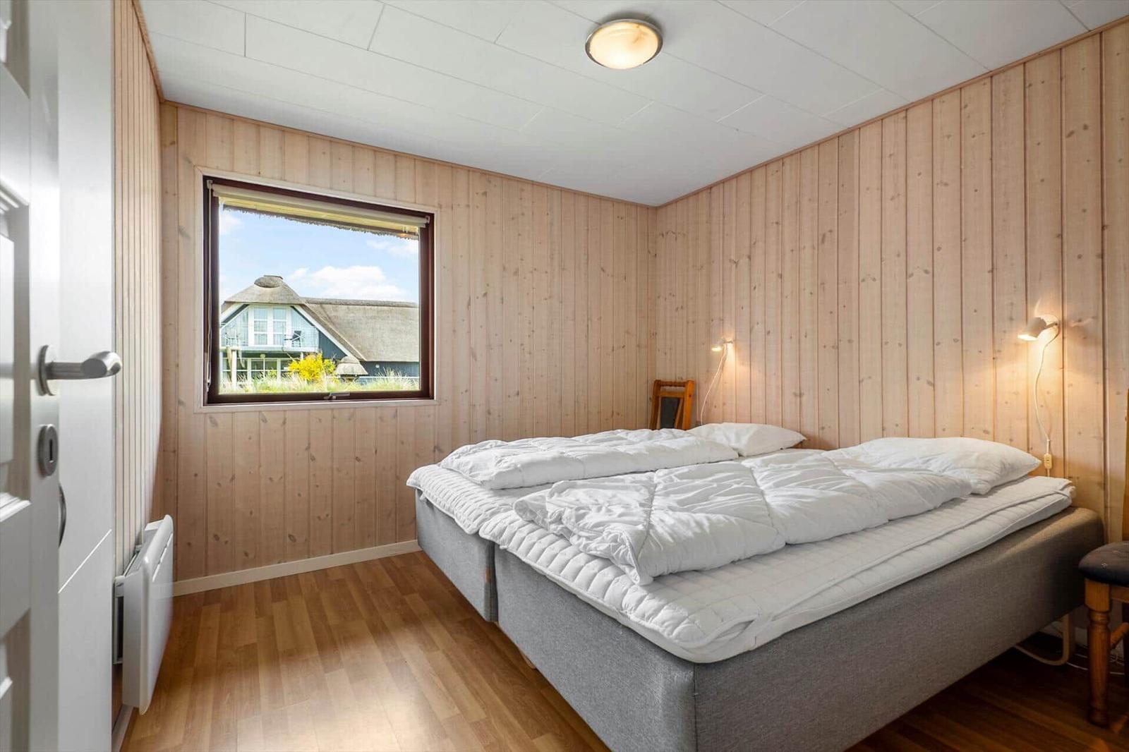 Schlafzimmer mit Holzwand, Bett und Fensterblick auf Haus.