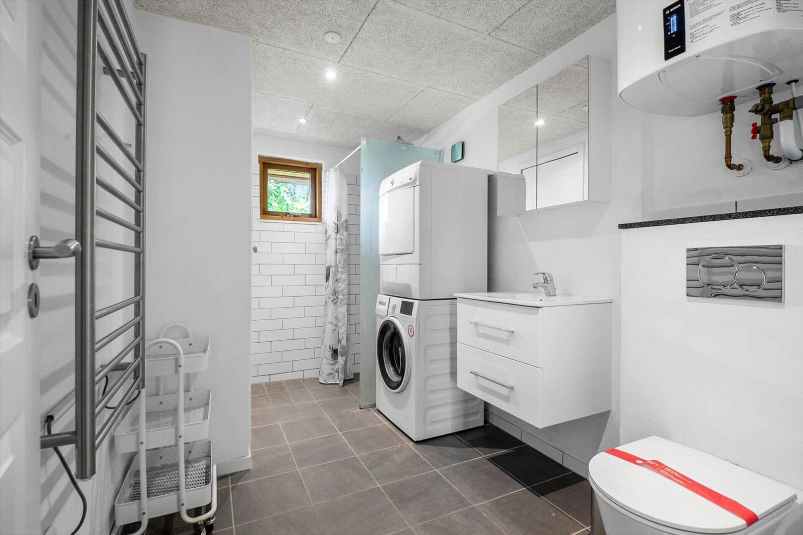 Badezimmer mit Waschmaschine, Spiegel, Toilette und Fenster.