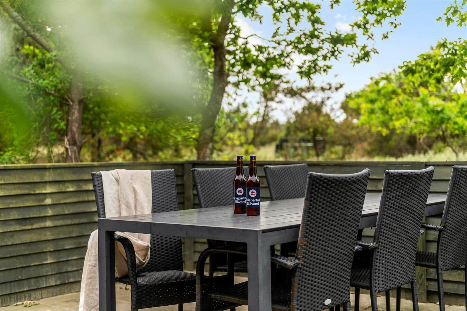 Terrasse mit Tisch und Stühlen, zwei Bierflaschen und Blick auf Bäume.