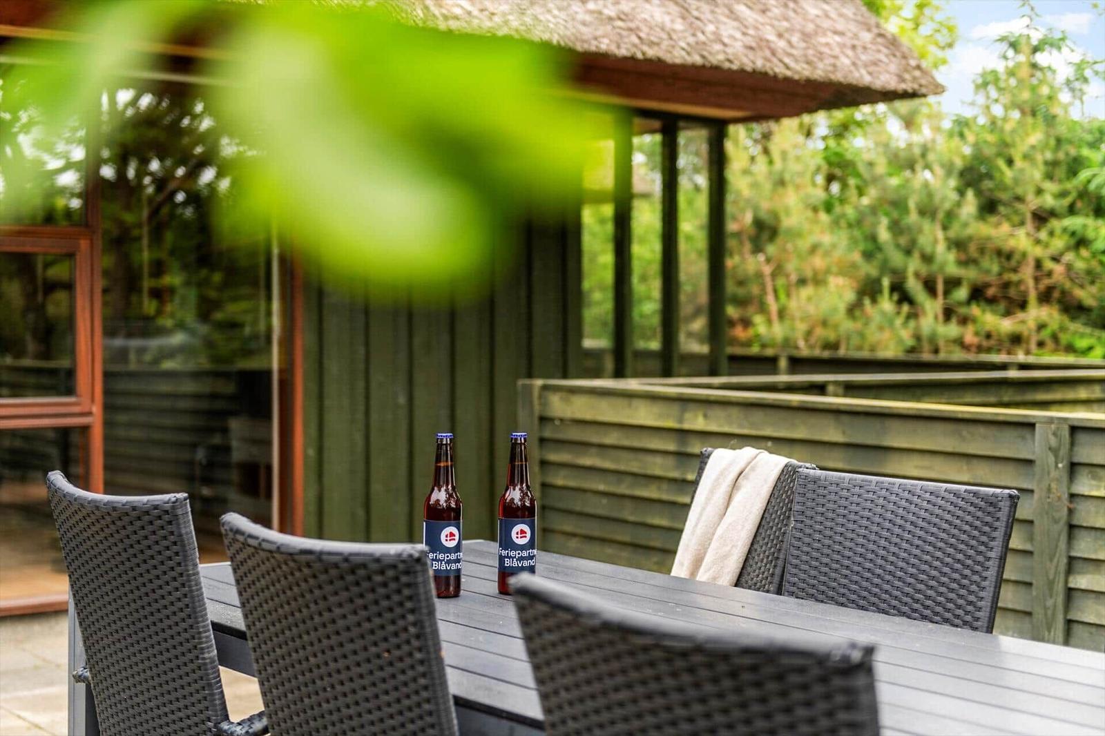 Terrasse mit Tisch, Stühlen und zwei Bierflaschen vor einem Holzhaus mit Dach.