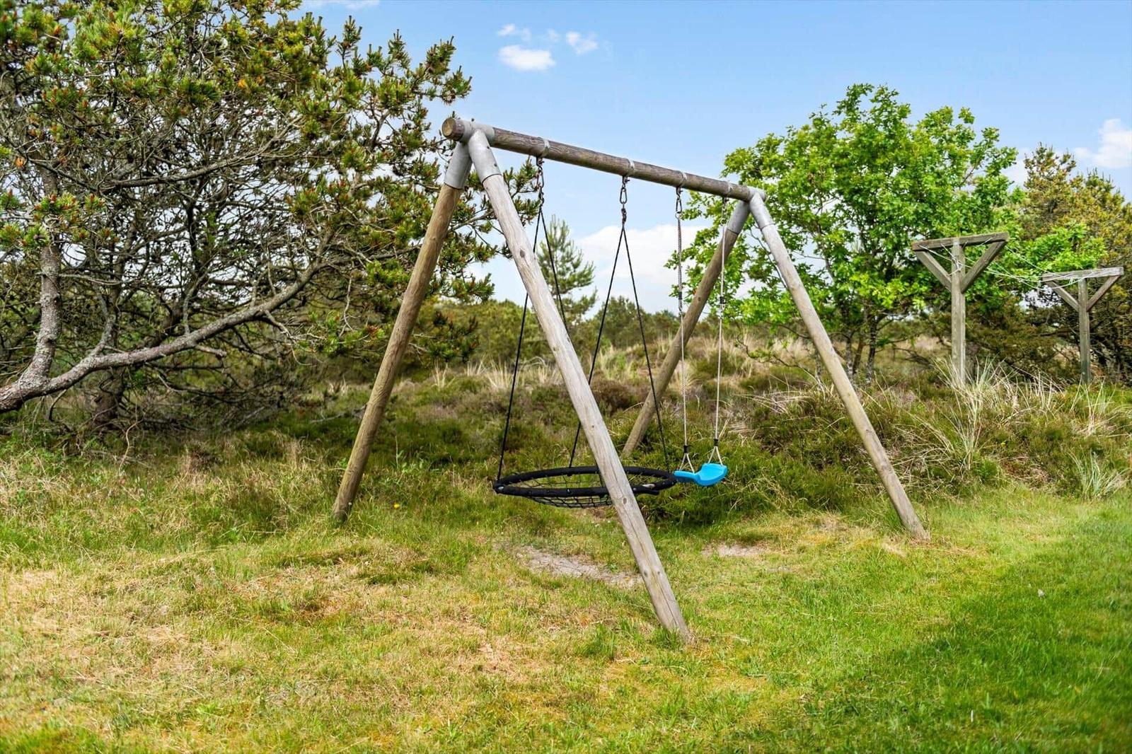 Holzschaukel mit blauem Sitz im Gras unter Bäumen