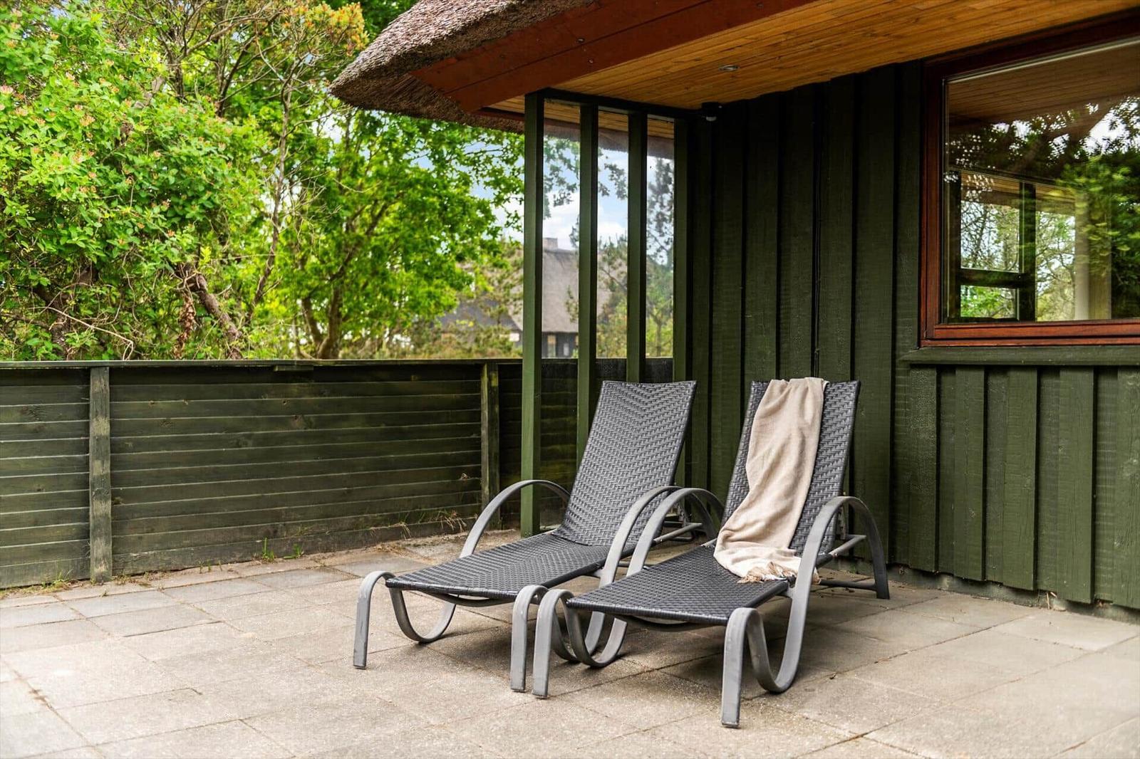 Zwei Liegestühle auf einer Terrasse vor einem Haus mit Holzwand und Dach.