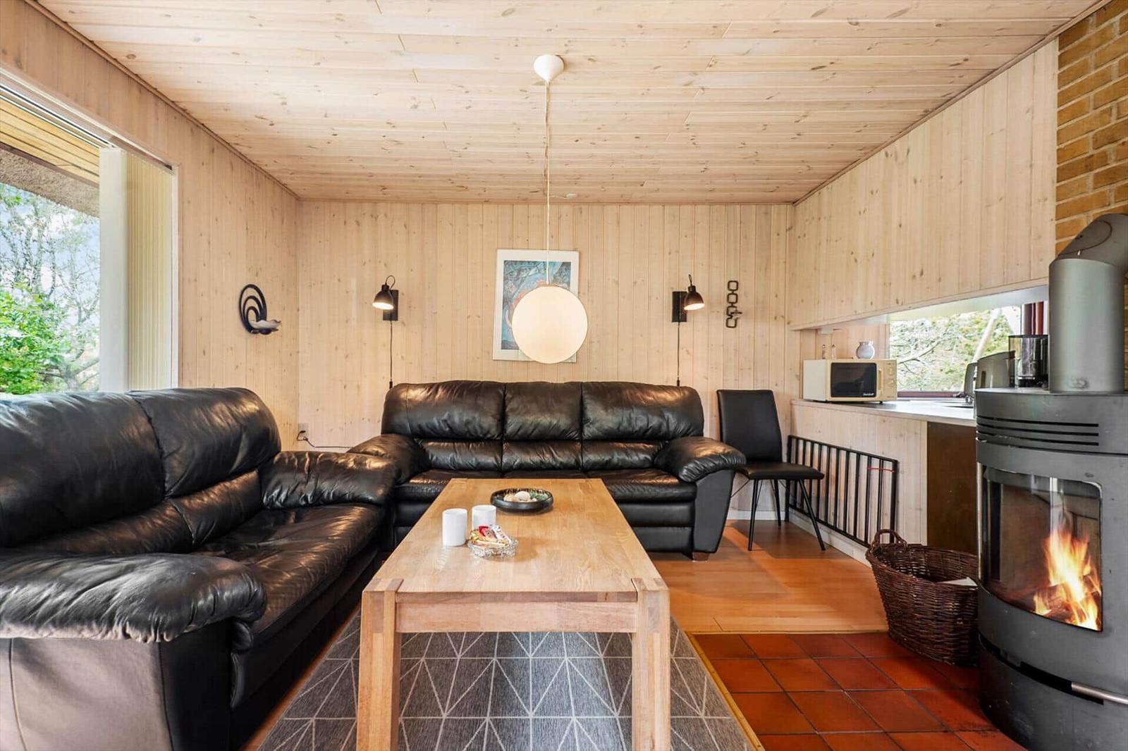Wohnraum mit Ledersofa, Holztisch und Kaminofen. Holzwände und -decke. Küche mit Mikrowelle.
