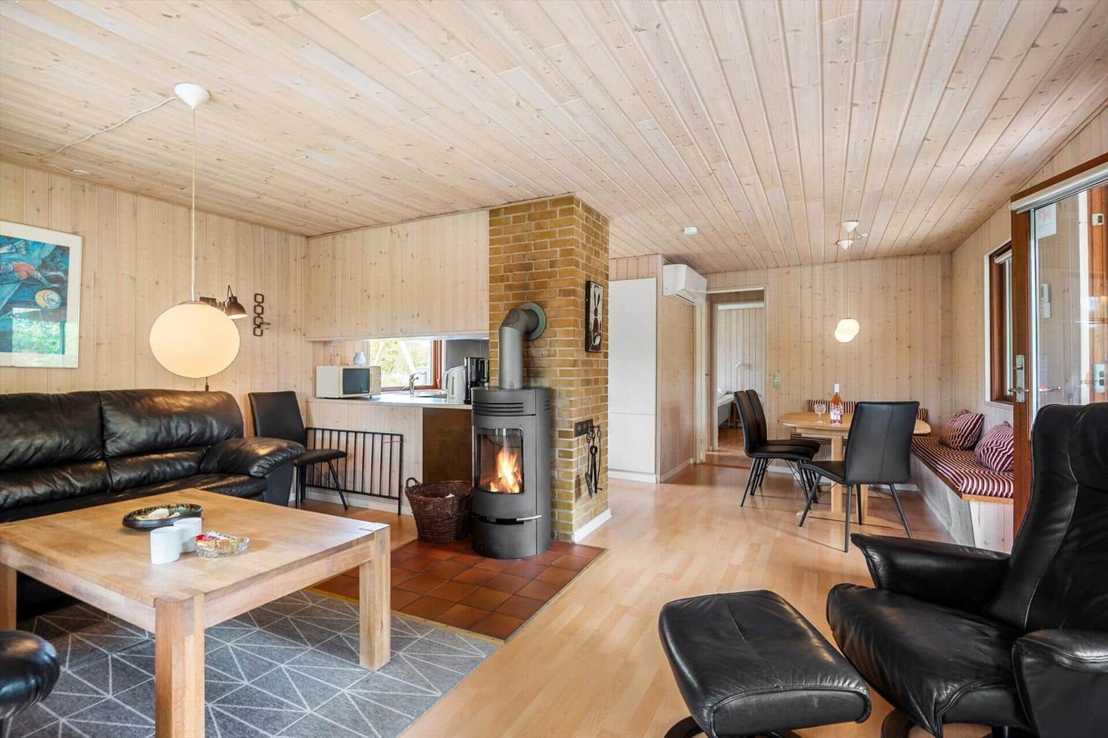 Wohnbereich mit Kamin, Sofa, Esstisch und Sitzbank. Holzdecke und -wände.