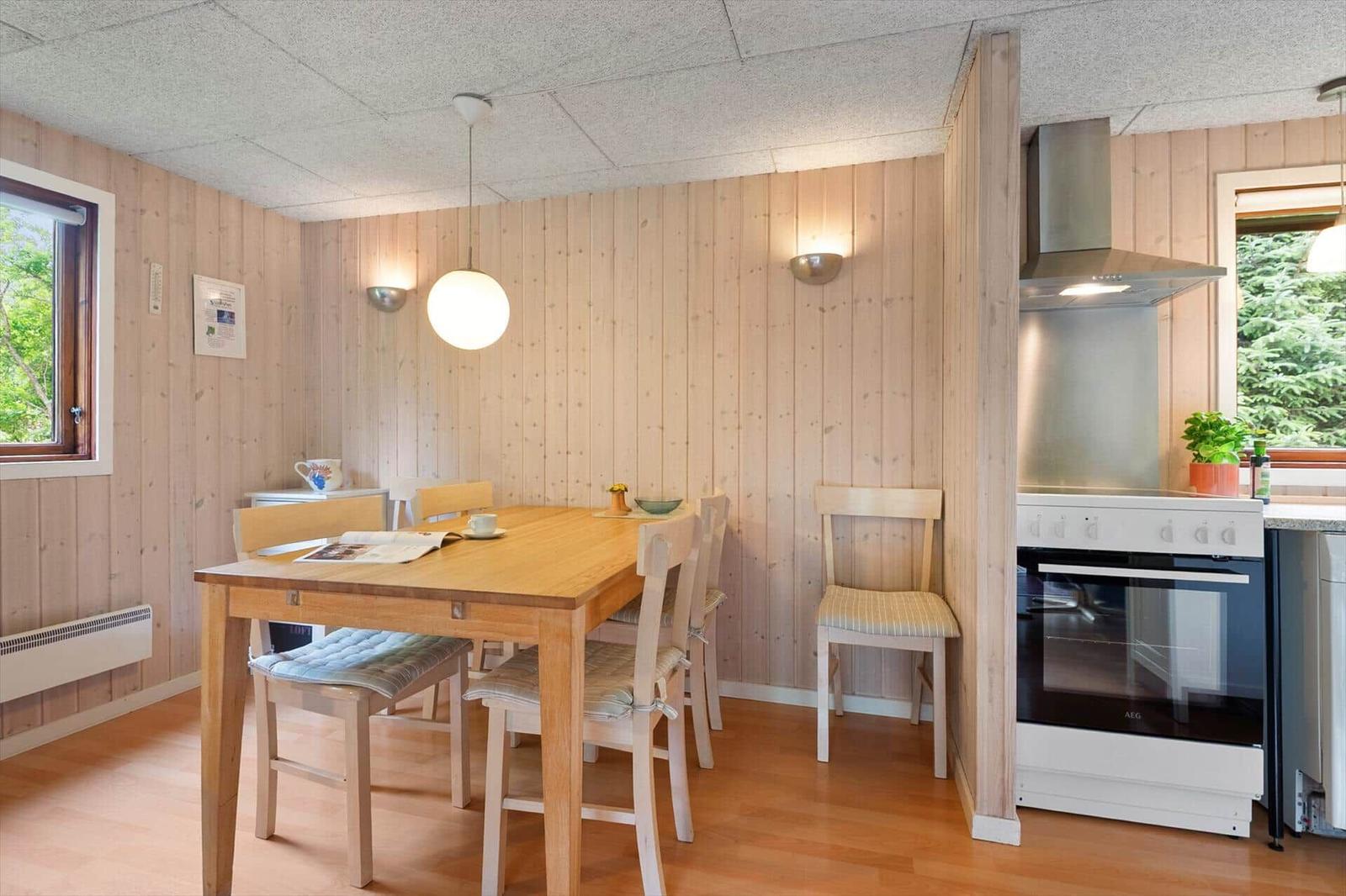 Esszimmer mit Holztisch, Stühlen und Küchenbereich mit Herd und Dunstabzug.