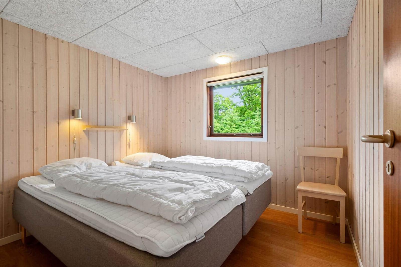 Schlafzimmer mit Doppelbett, Holzwandverkleidung und Fenster mit Blick auf Bäume.
