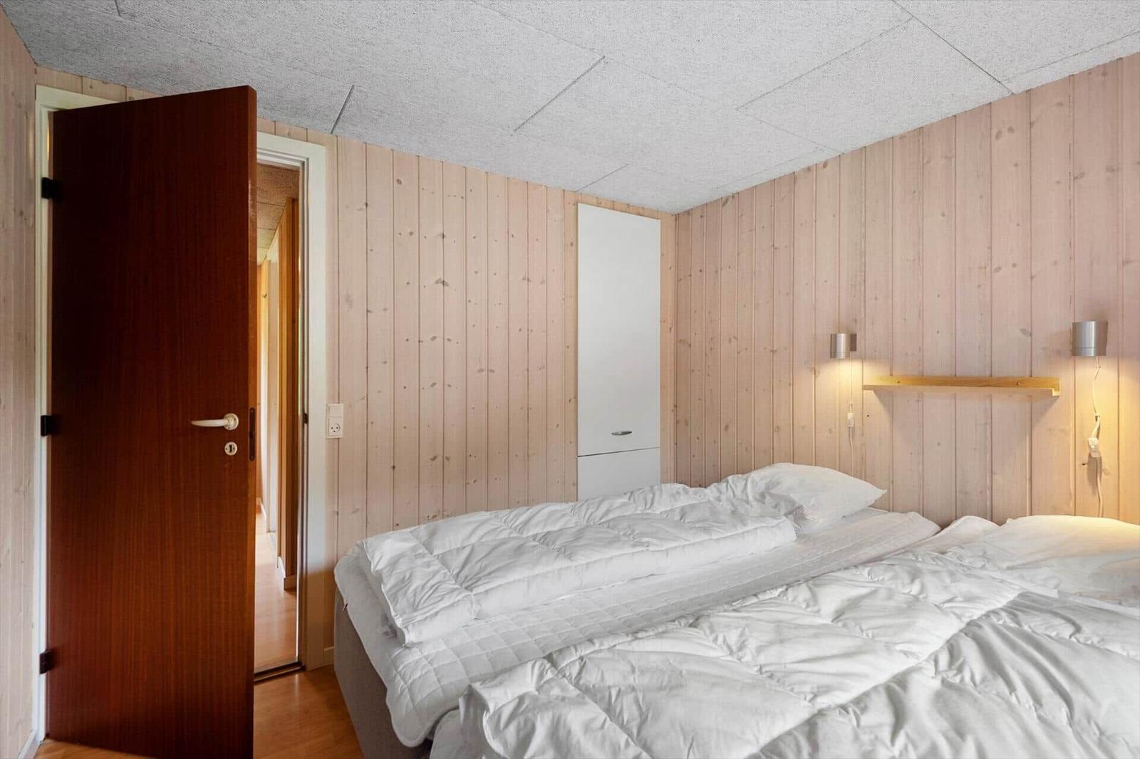 Schlafzimmer mit Holzwand, Bett und Schrank. Tür führt in einen Flur.