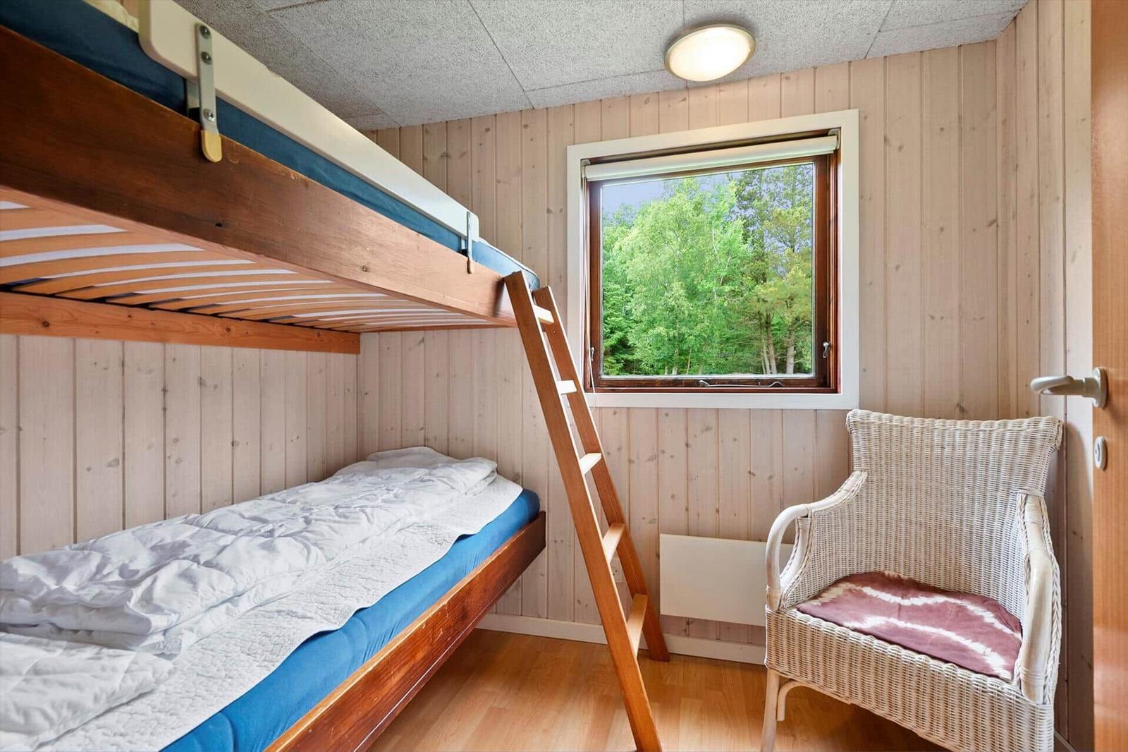 Zimmer mit Doppelstockbett, Fenster mit Waldblick und Stuhl.