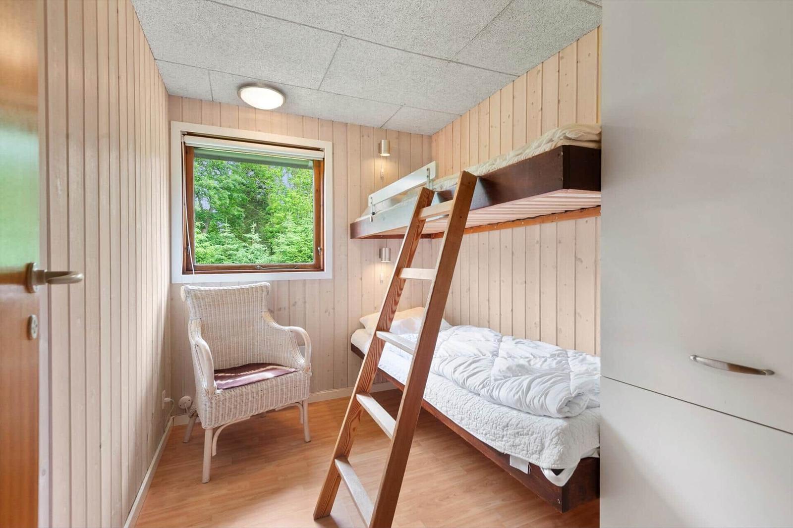 Zimmer mit Doppelstockbett, Stuhl und Fenster mit Blick auf Wald.