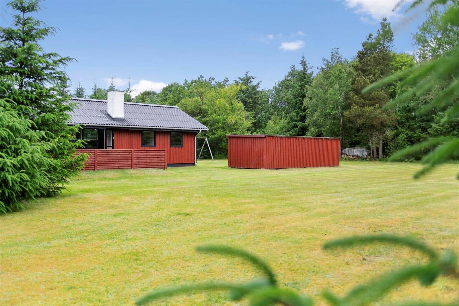 Rotes Ferienhaus mit Garten und Wald im Hintergrund.