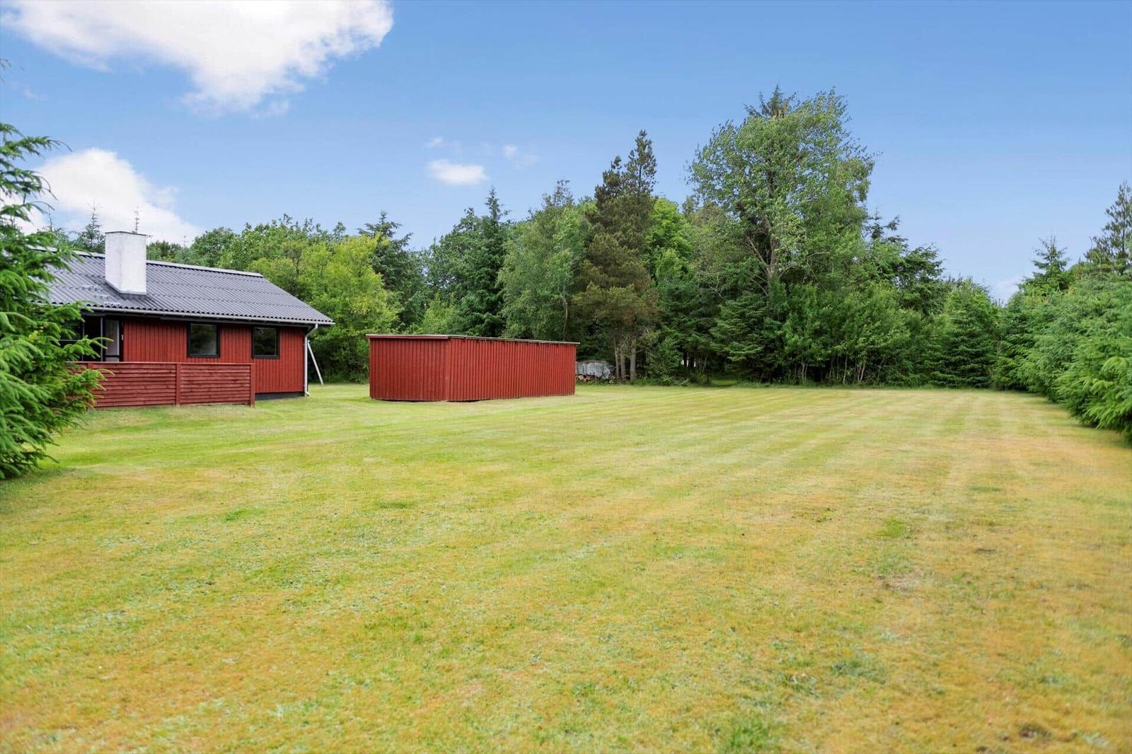 Roter Holzhaus mit Garten und Wald im Hintergrund.