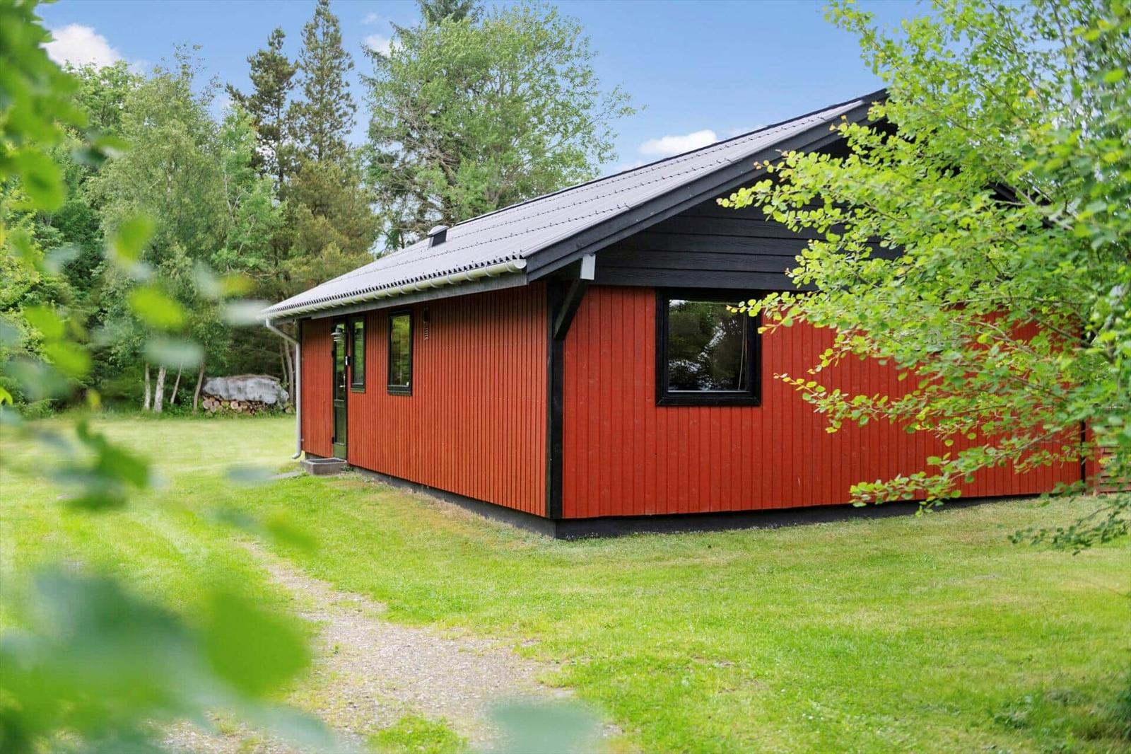 Rotes Holzhaus mit schwarzem Dach in grüner Umgebung.