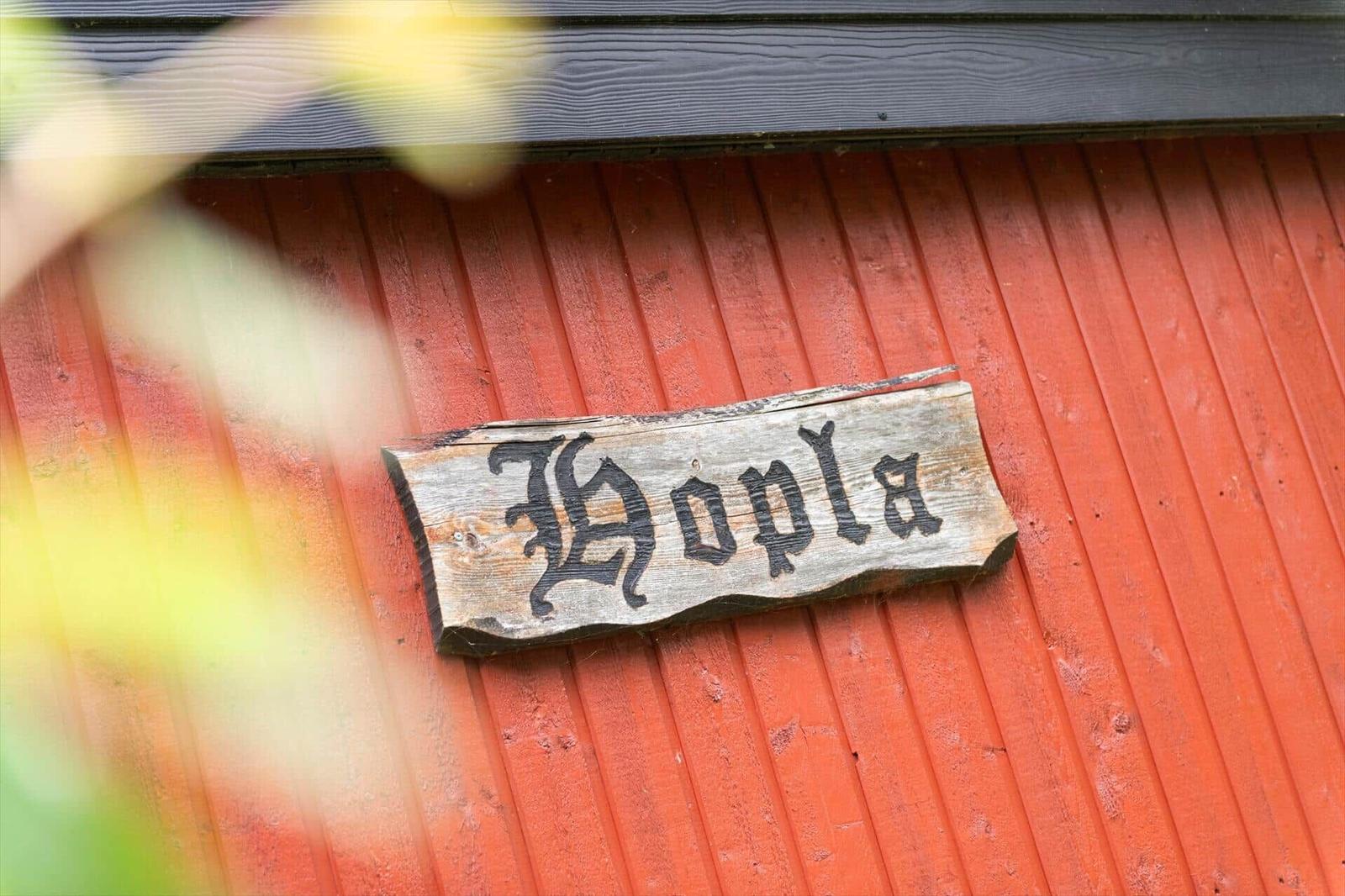 Holzschild mit Schriftzug Hopla an roter Holzwand.
