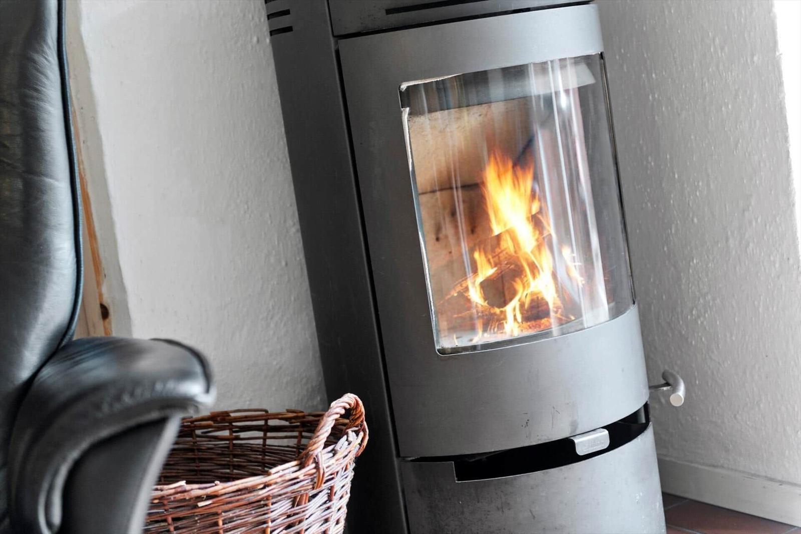 Moderne Holzofen mit brennendem Feuer, daneben Sessel und Korb.