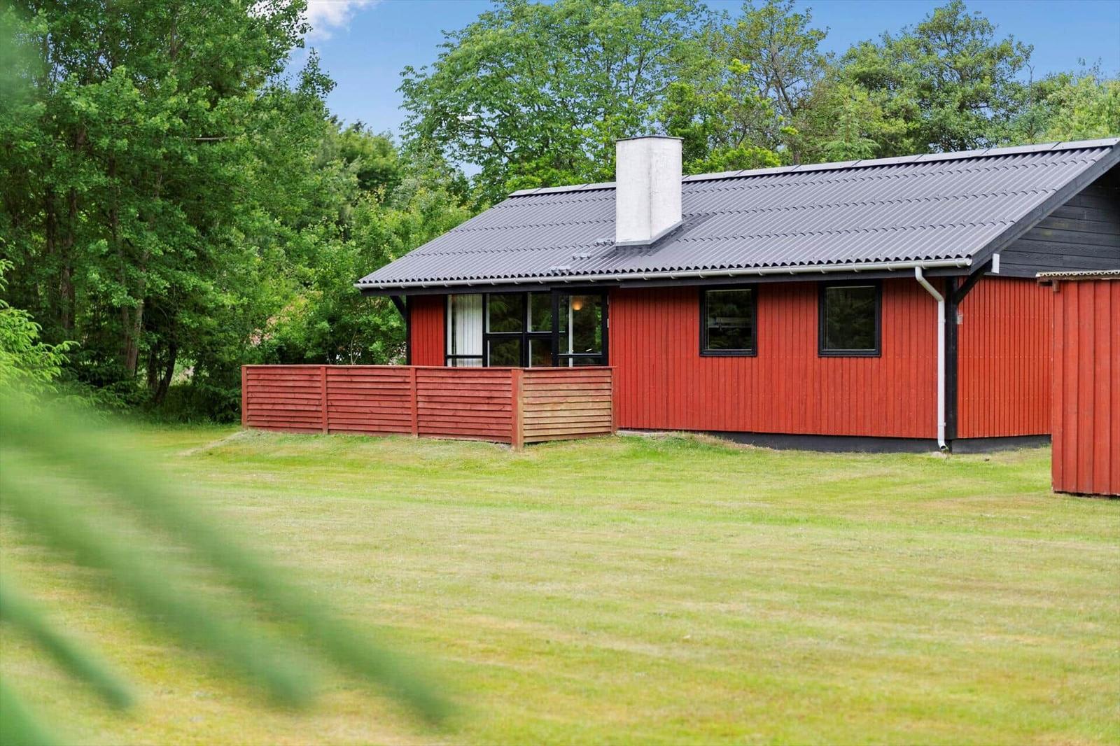 Rotes Holzhaus mit grauem Dach und Garten. Umgeben von Bäumen und Gras.