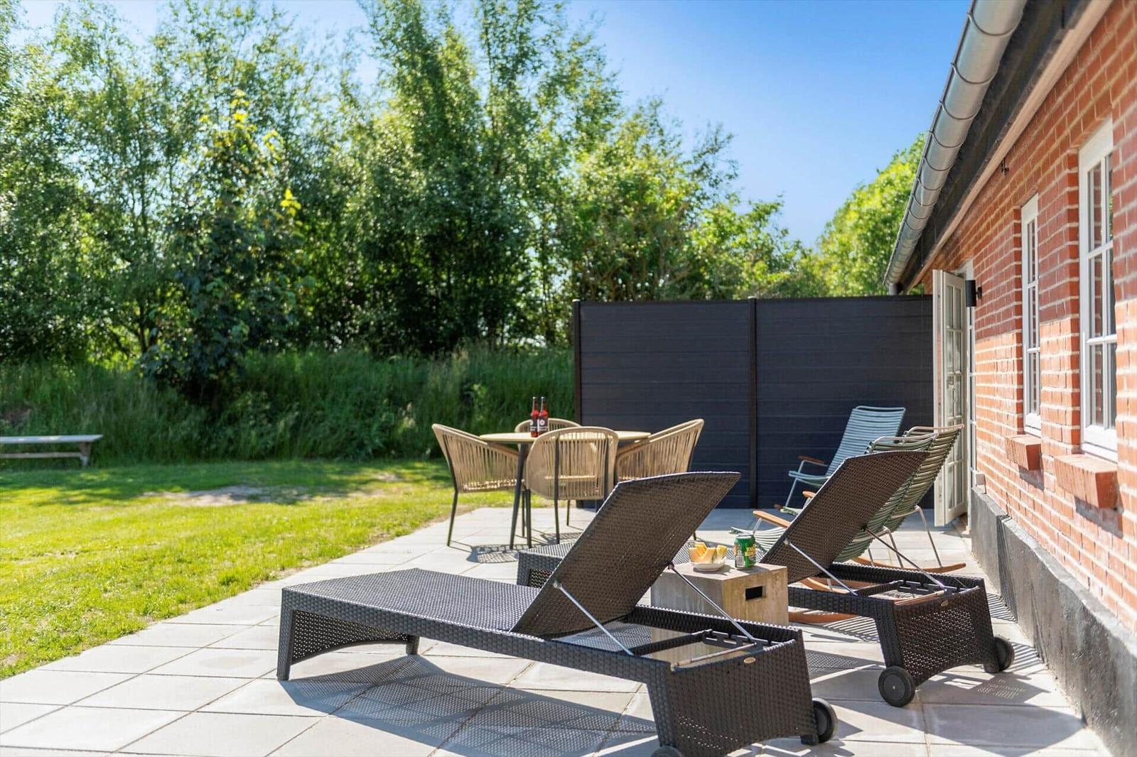 Terrasse mit Liegen, Tisch und Stühlen neben einem roten Backsteinhaus.